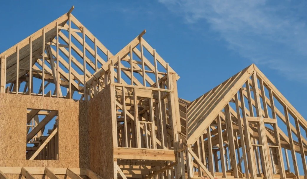 Wooden framing of a house under construction with blue sky in the background.