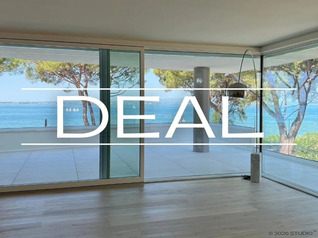Modern living room with large floor-to-ceiling windows overlooking the ocean, with trees and sailboats visible outside, and the word "DEAL" superimposed in the center.