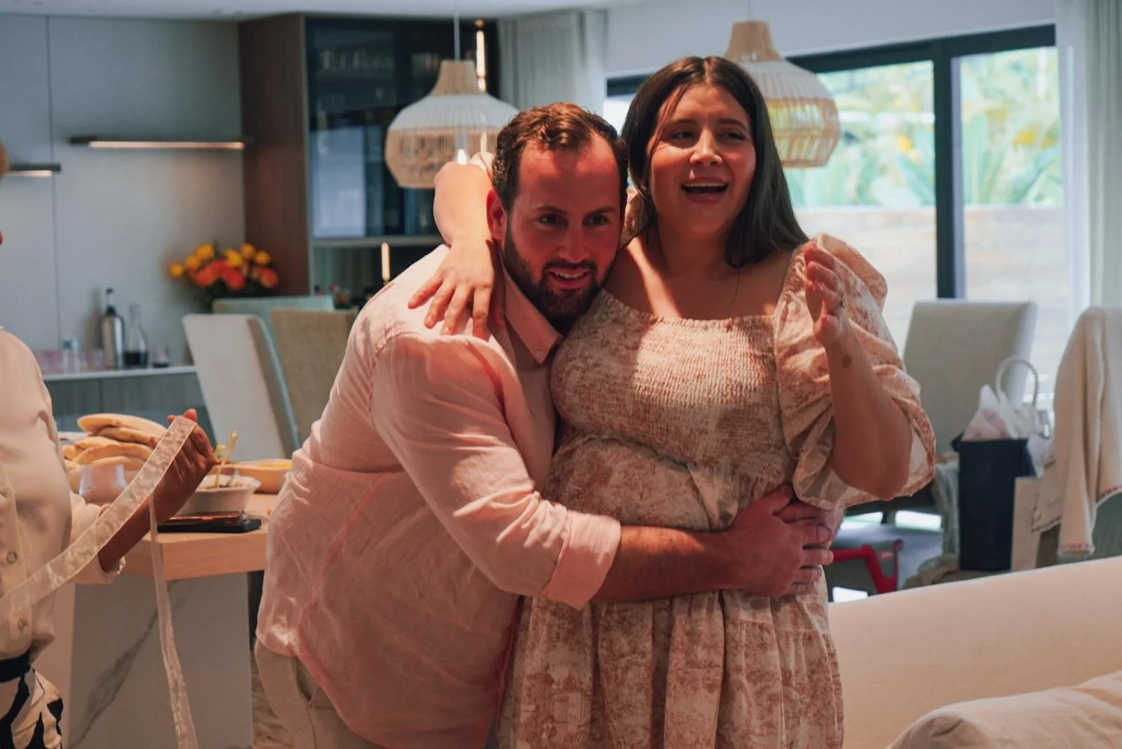 A man and woman embrace and smile in a well-lit dining room, celebrating together.