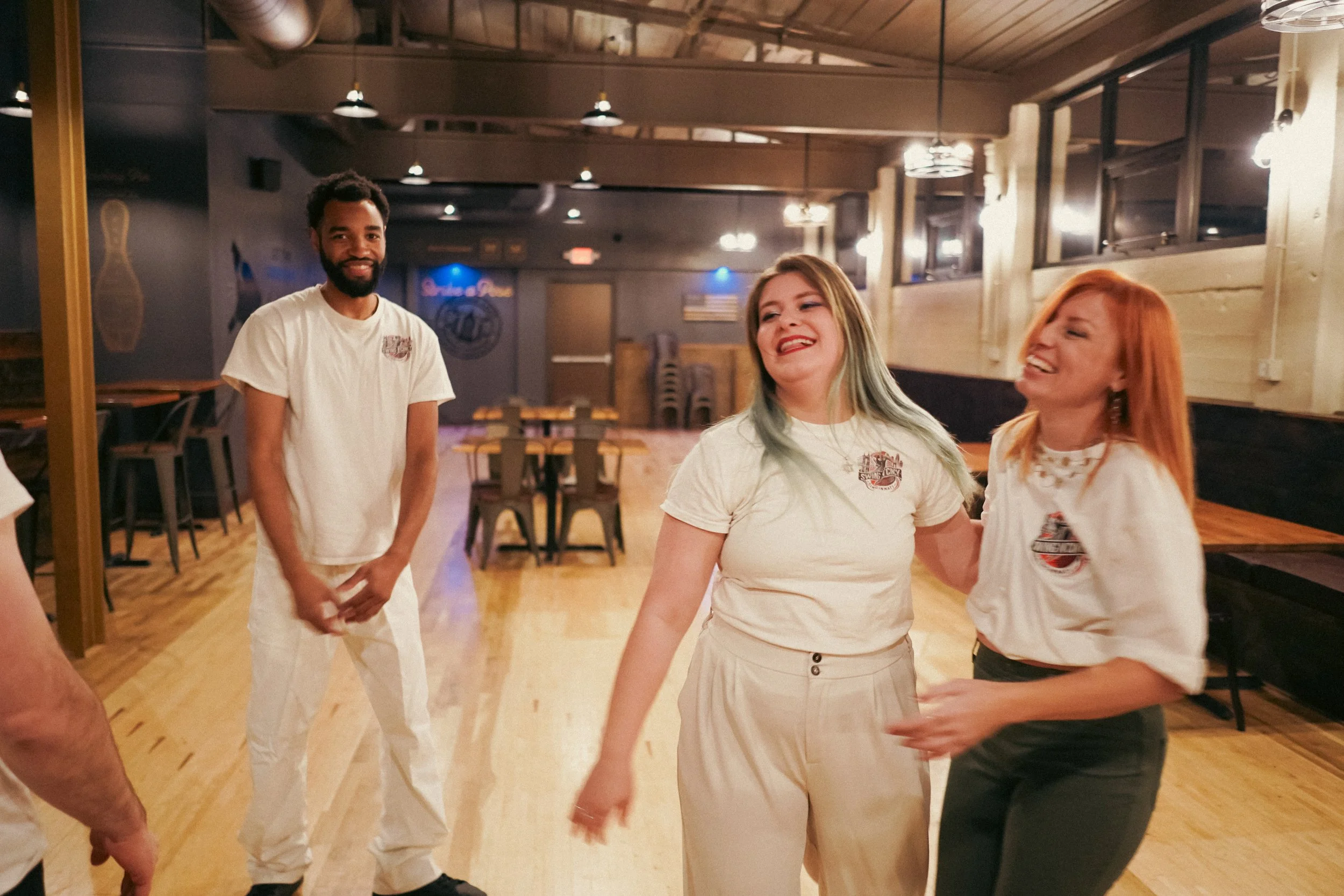 Three people in a restaurant, smiling and laughing. One man in white on the left, a woman with green hair in the center, and a red-haired woman on the right.