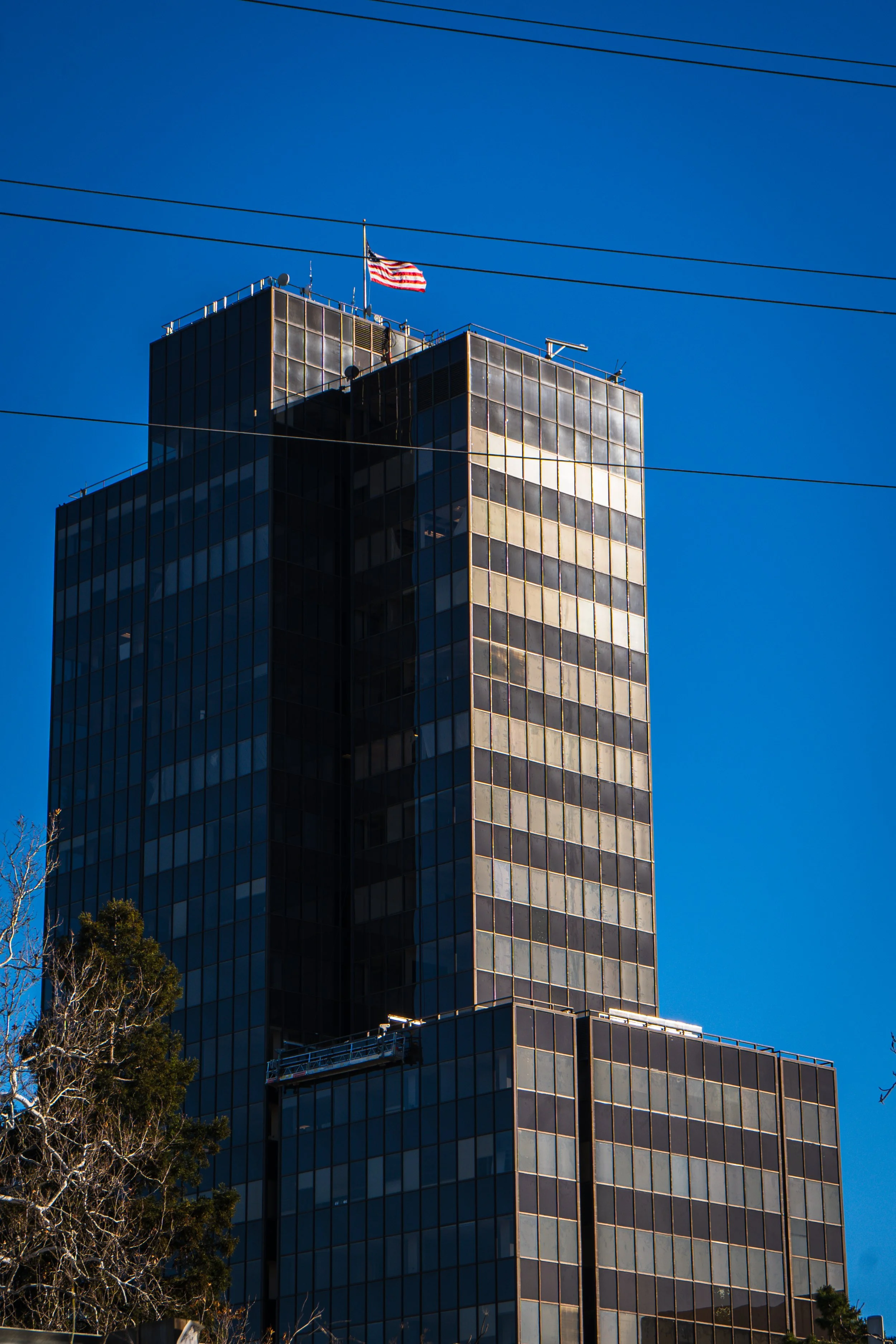 Pruneyard Tower in Campbell with reflective windows and an American flag on top, against a clear blue sky.