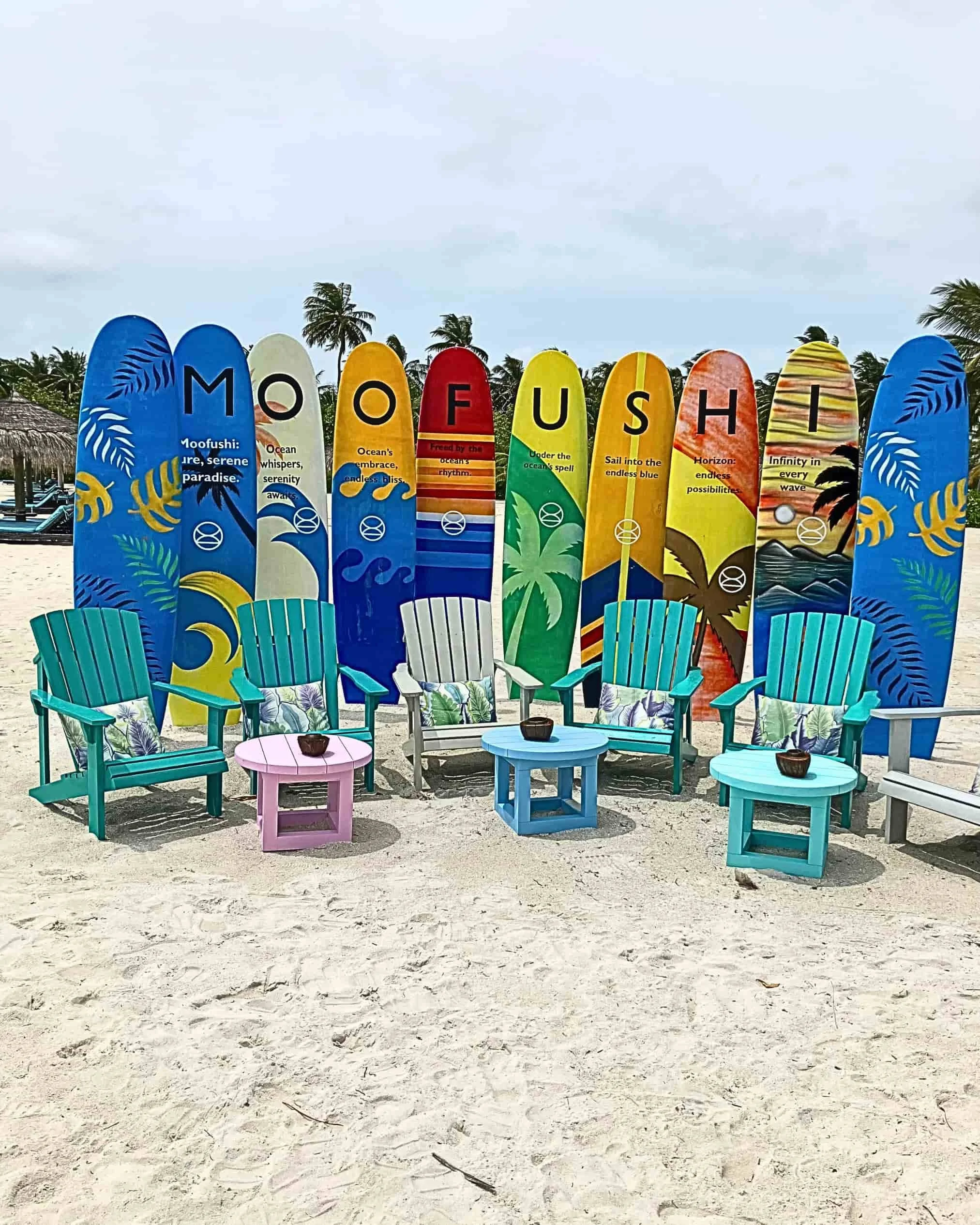 Colorful tropical surfboards and beach chairs on the sand at Constance Moofushi Maldives.