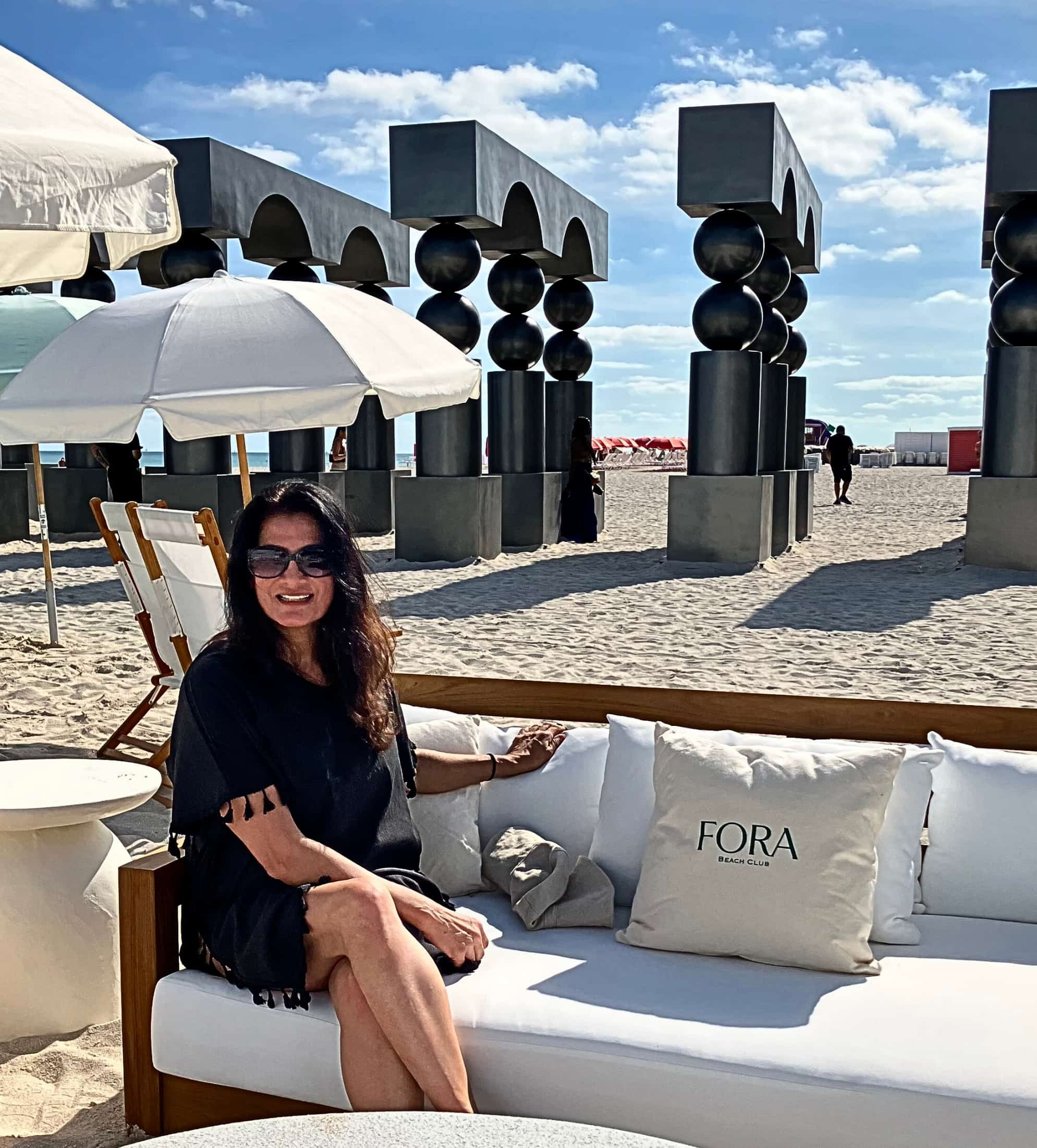 Anjali Augustine relaxing oceanside at the Fora Beach Club at The Shelborne Miami, surrounded by art installations during Art Week in Miami
