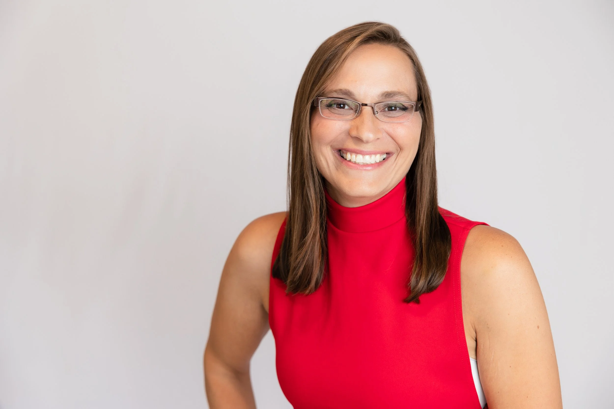 Woman with brown hair wearing glasses and a sleeveless red top, smiling against a plain white background.