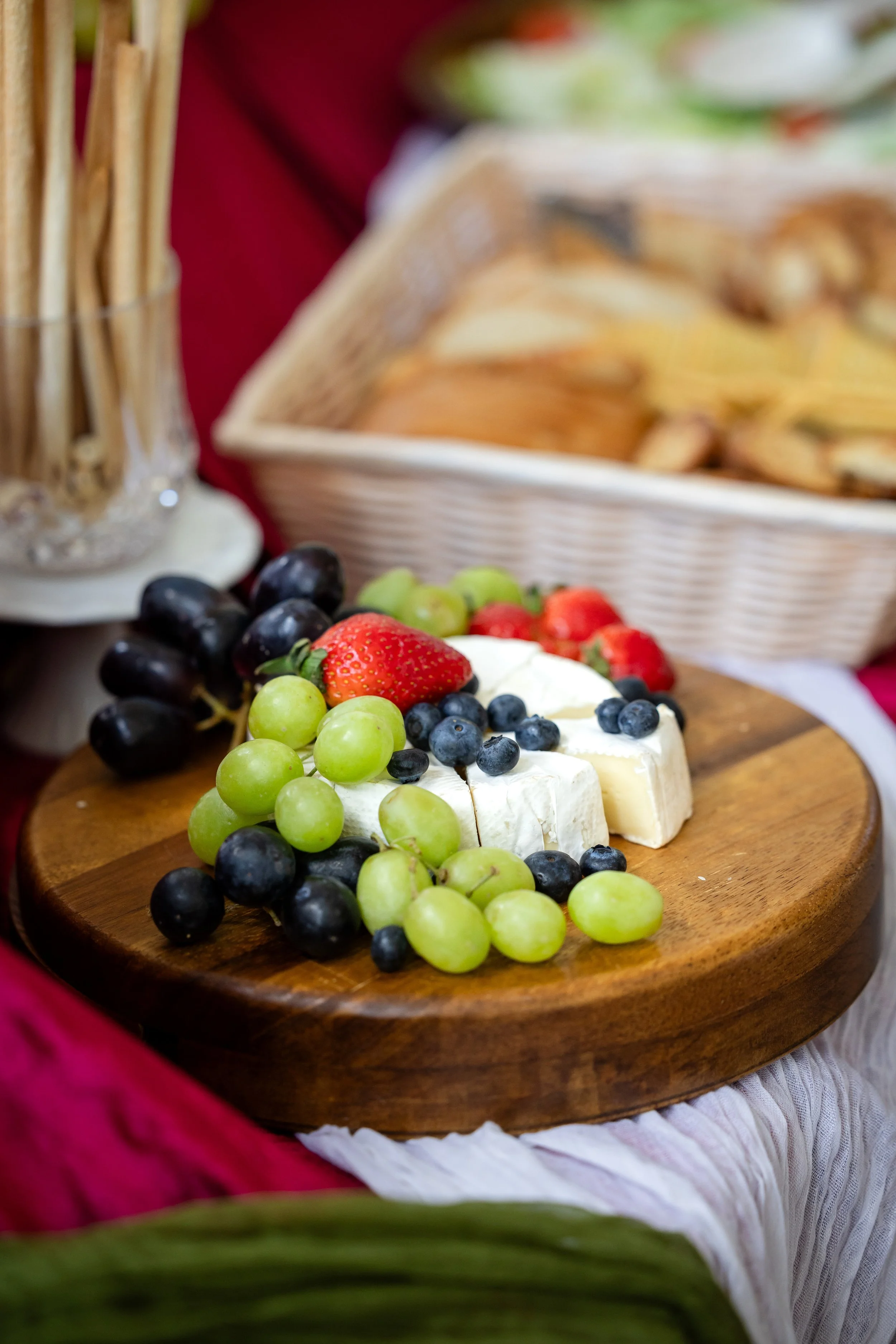 Close-up of a cheese platter topped with green grapes, black grapes, strawberries, and blueberries, placed on a wooden serving board.