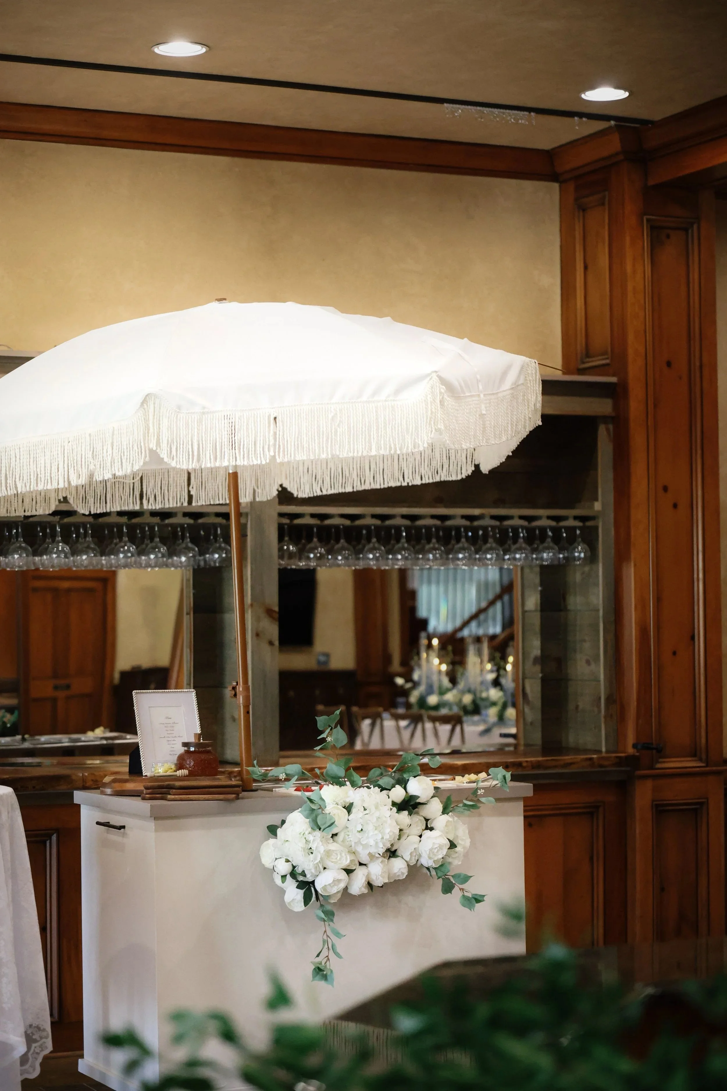 A floral arrangement of white roses and greenery on a counter with a white cover, set in a rustic venue with wooden decor and a large mirror.