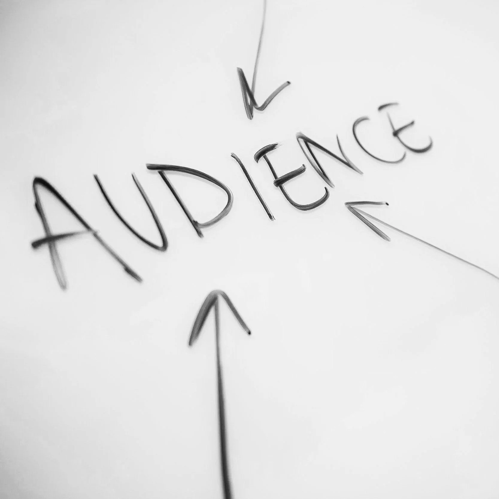 Handwritten word 'AUDIENCE' with arrows pointing in four directions on a white surface.