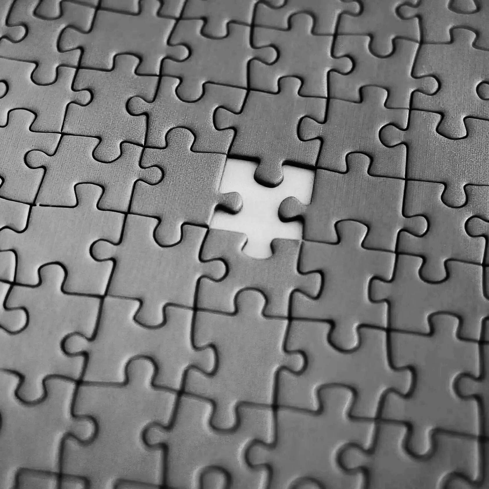 A black and white photograph of a nearly completed jigsaw puzzle with one missing piece in the center.