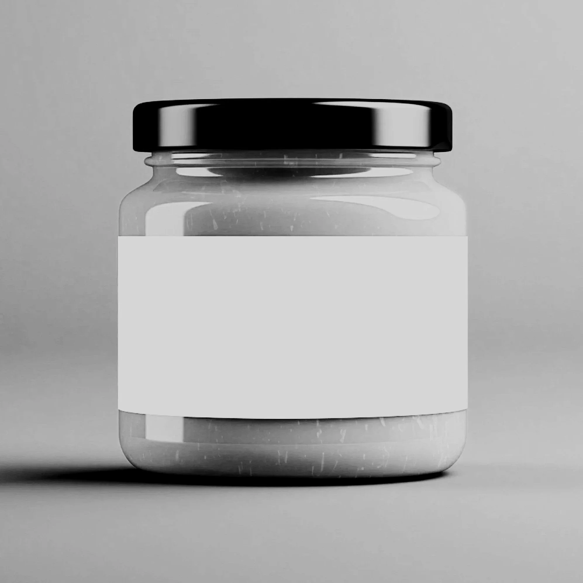A black and white photo of a glass jar with a black lid and a blank white label on the front, sitting on a flat surface against a plain background.