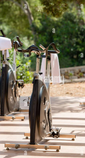 Stationary exercise bike positioned outdoors on a gravel surface with trees and greenery in the background. A great space next to nature to workout and get re-energized.  TK Glamping and Wellness in Vernon BC.