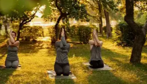 Three women practicing yoga outdoors on mats in a garden with trees and bushes. It is a beautiful day, bright and sunny closer to sunset with shadows casting on the ground.  TK Glamping and Wellness in Vernon BC.