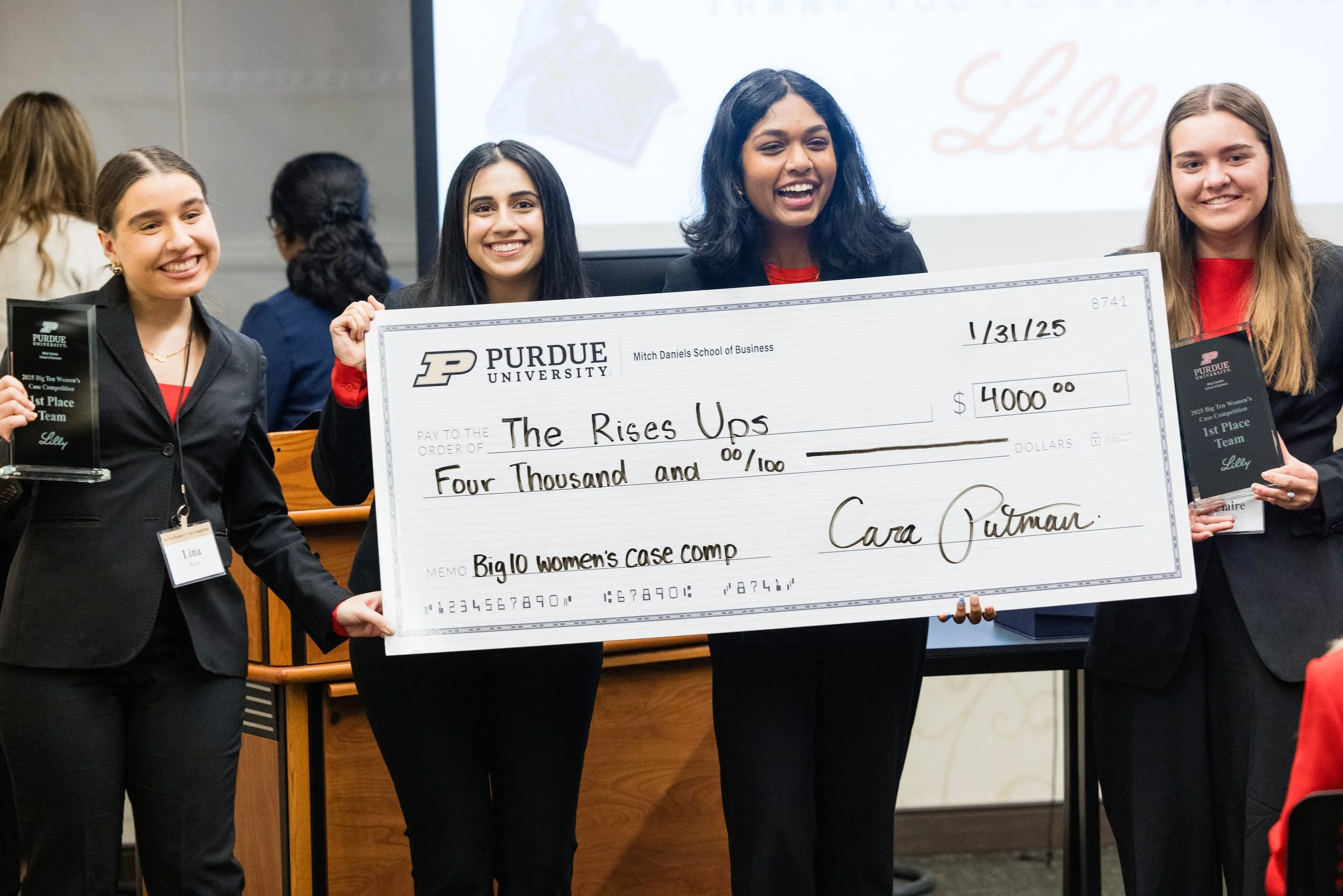 Group of four young women on stage holding a large check and awards, celebrating their victory at Purdue University