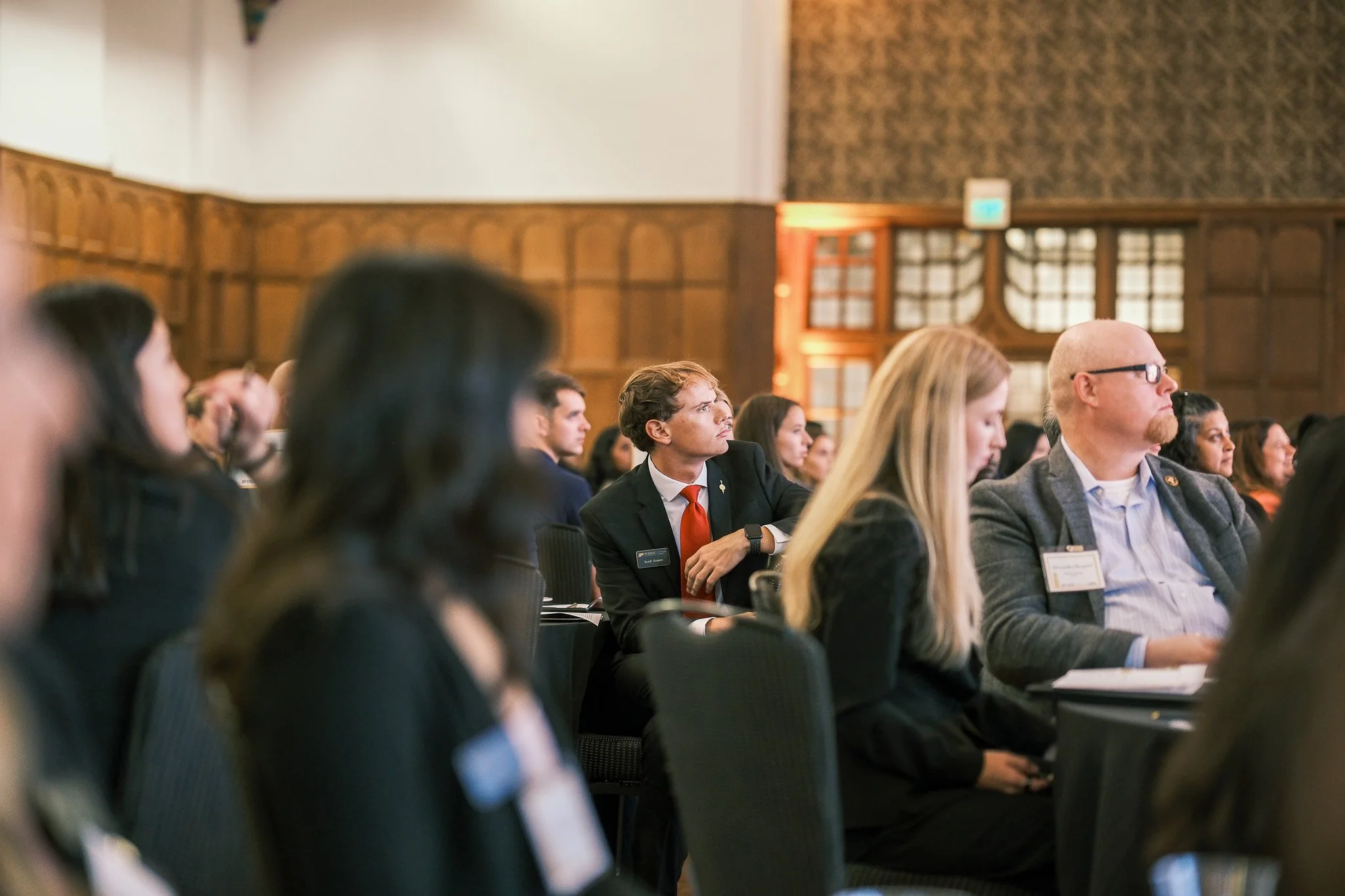 Audience at a conference listening attentively in a wood-paneled room.