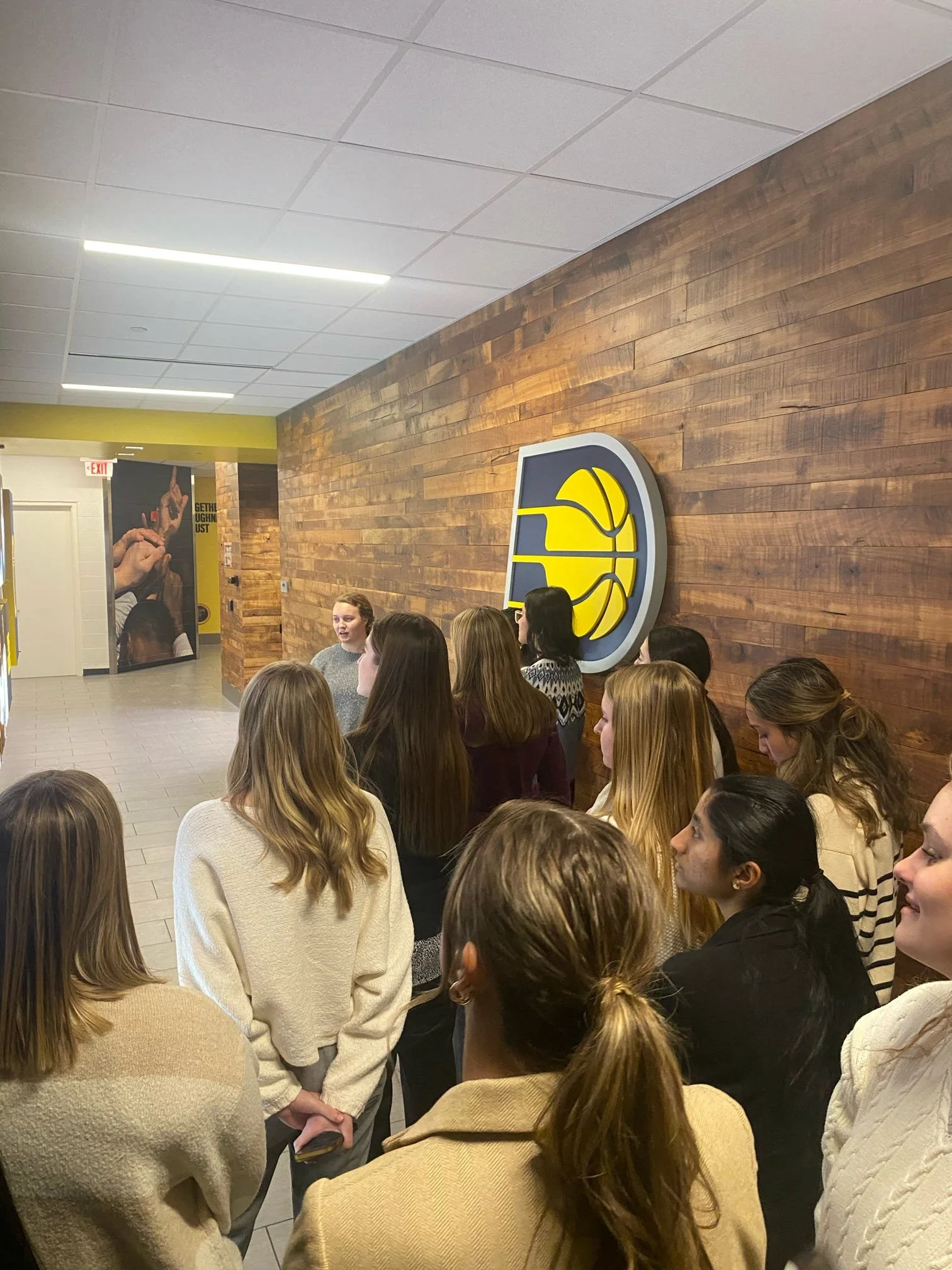 Group of young women standing in line at a basketball team store or event, with a Utah Jazz logo on the wall behind them.