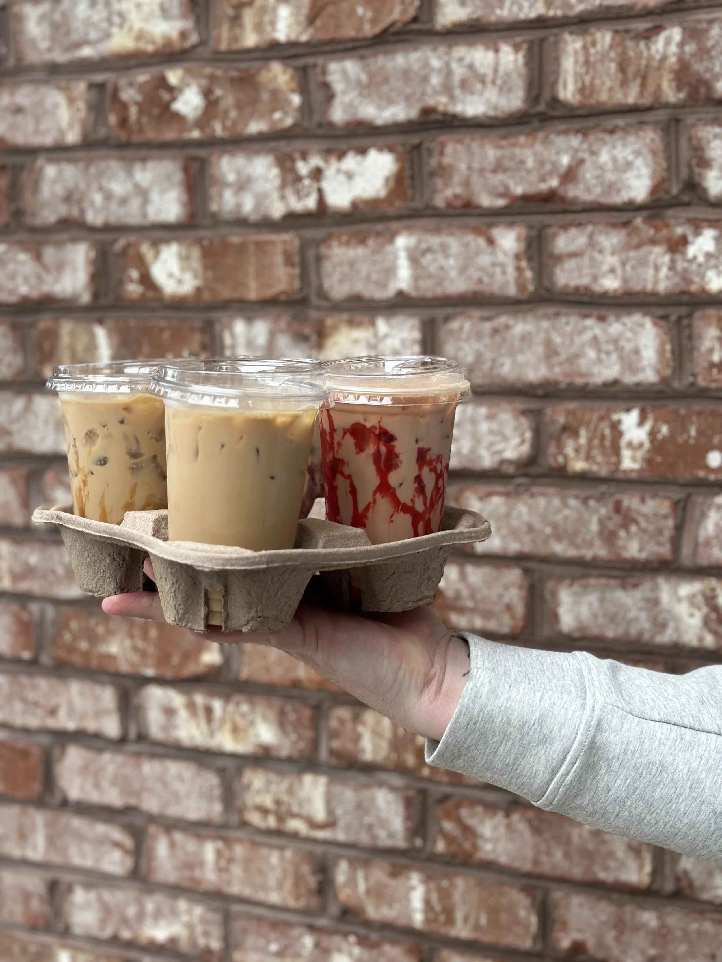 A hand holds a coffee cup carrier with iced coffee beverages