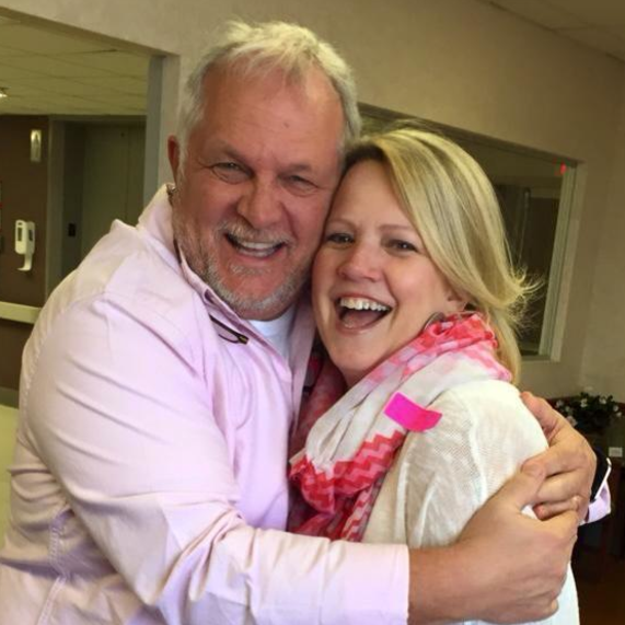 A man and woman hug while looking at the camera.
