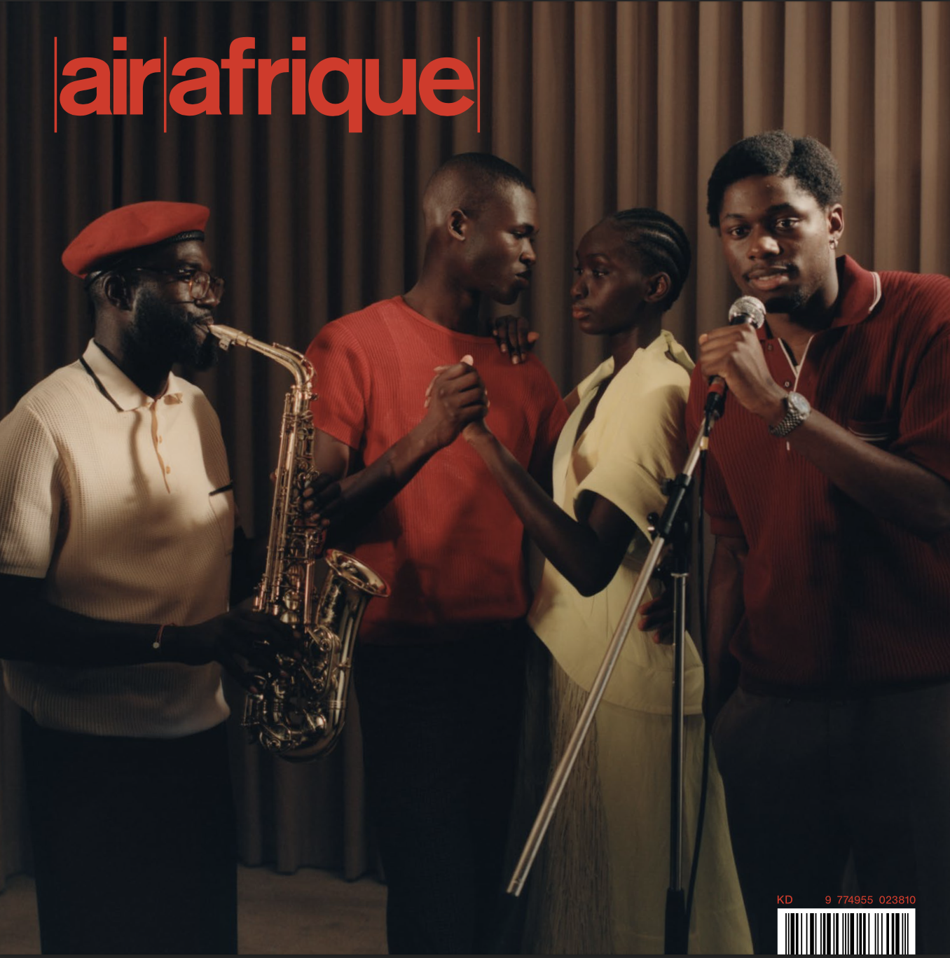 Cinq personnes sur scène, dont une joue du saxophone, tandis que deux autres se regardent intensément et une personne chante dans un micro, devant un rideau. Cover du Magazine Air Afrique