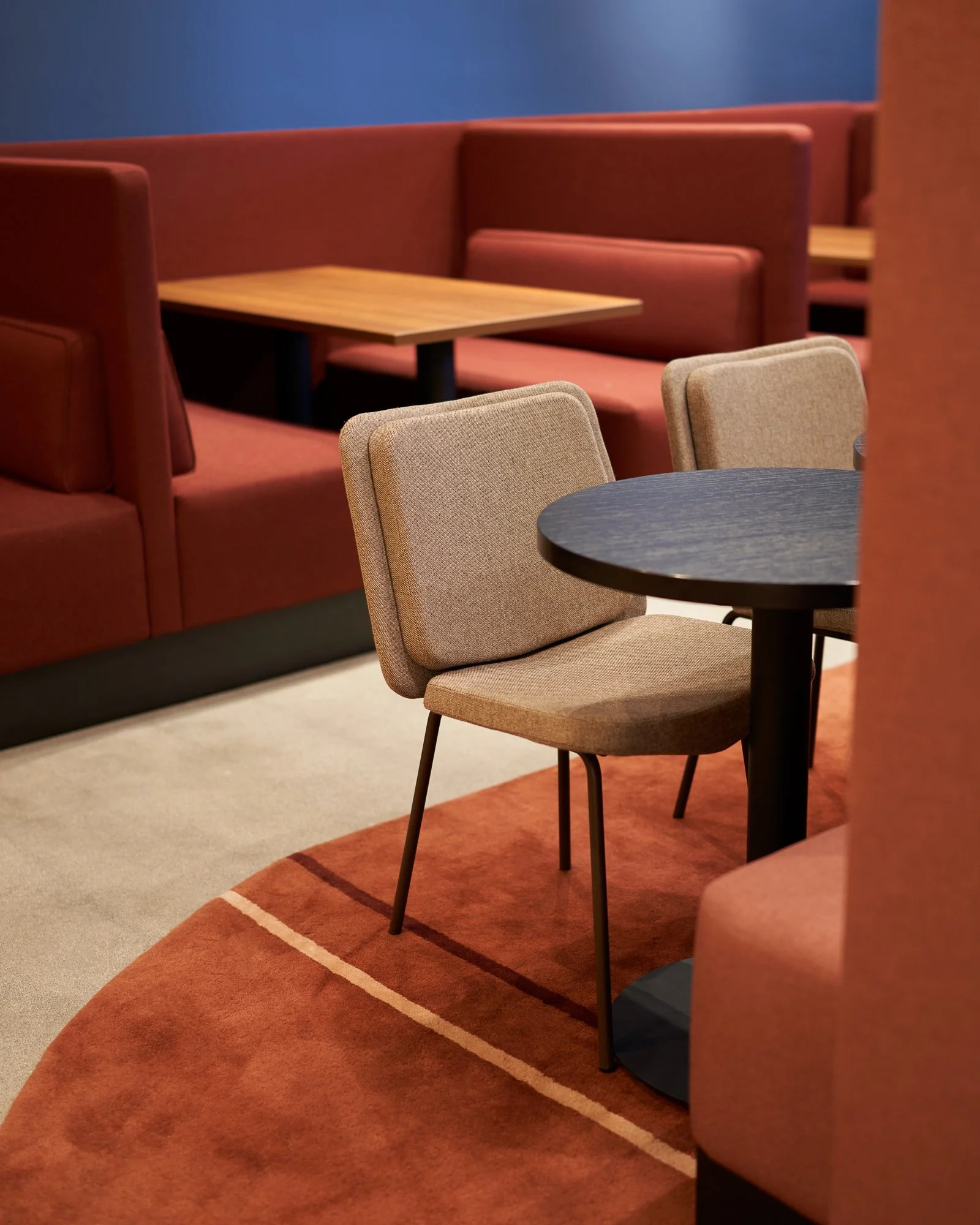 Empty dining area with beige and brown chairs, round black table, and booth seating with orange cushions and orange backs in a modern restaurant.