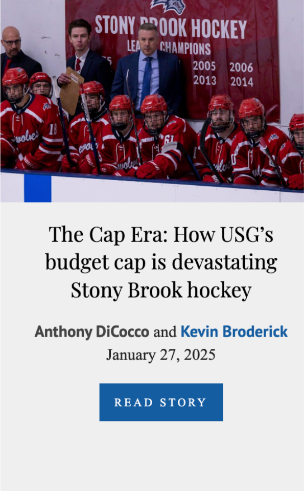Hockey team in red uniforms and helmets sitting on the bench, with coaches standing behind them, at the Stony Brook hockey team event.