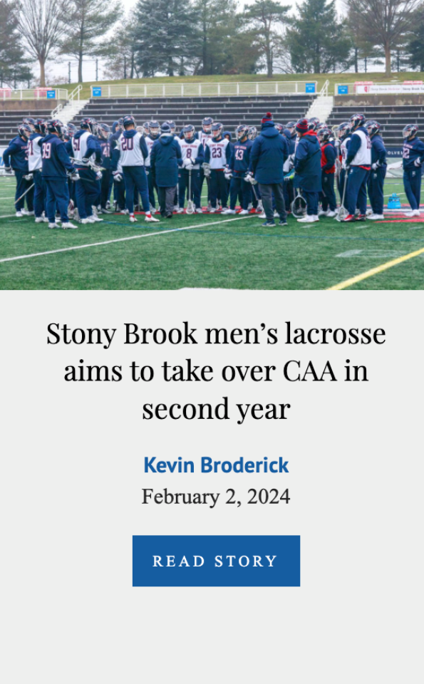 A group of Stony Brook men's lacrosse players and coaches gathered on a football field during daytime for a team meeting or discussion, with empty bleachers and trees in the background.
