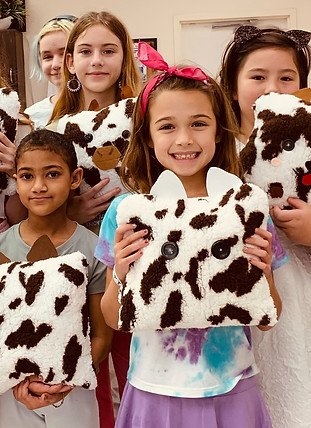 Five young girls holding cow-shaped plush toys in a room with a white door.
