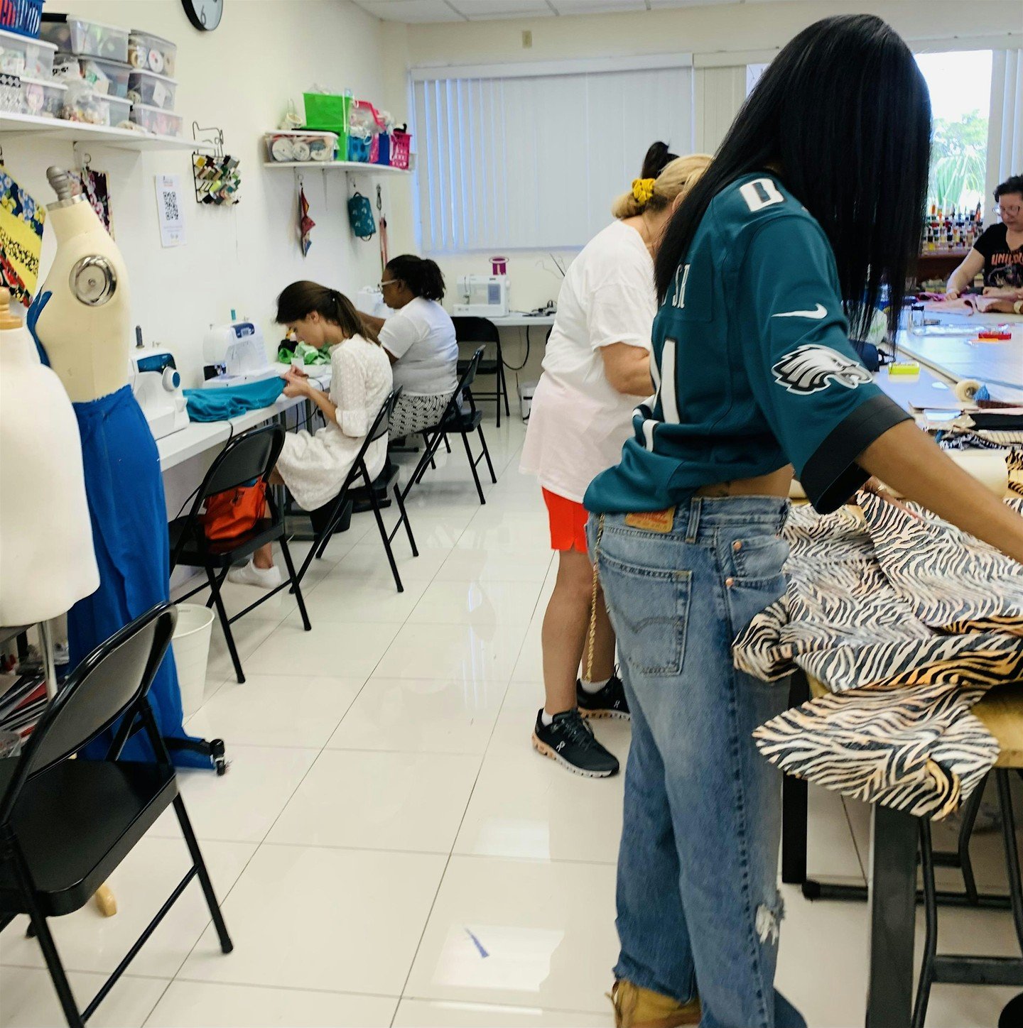 People working on sewing projects in a craft room, with sewing machines and fabric.