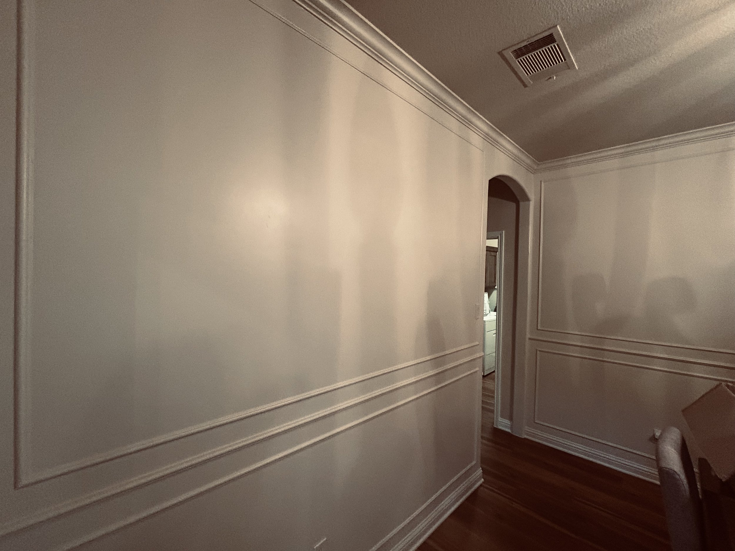 Empty dining room with white walls, decorative molding, hardwood floor, and an open doorway leading to a kitchen.