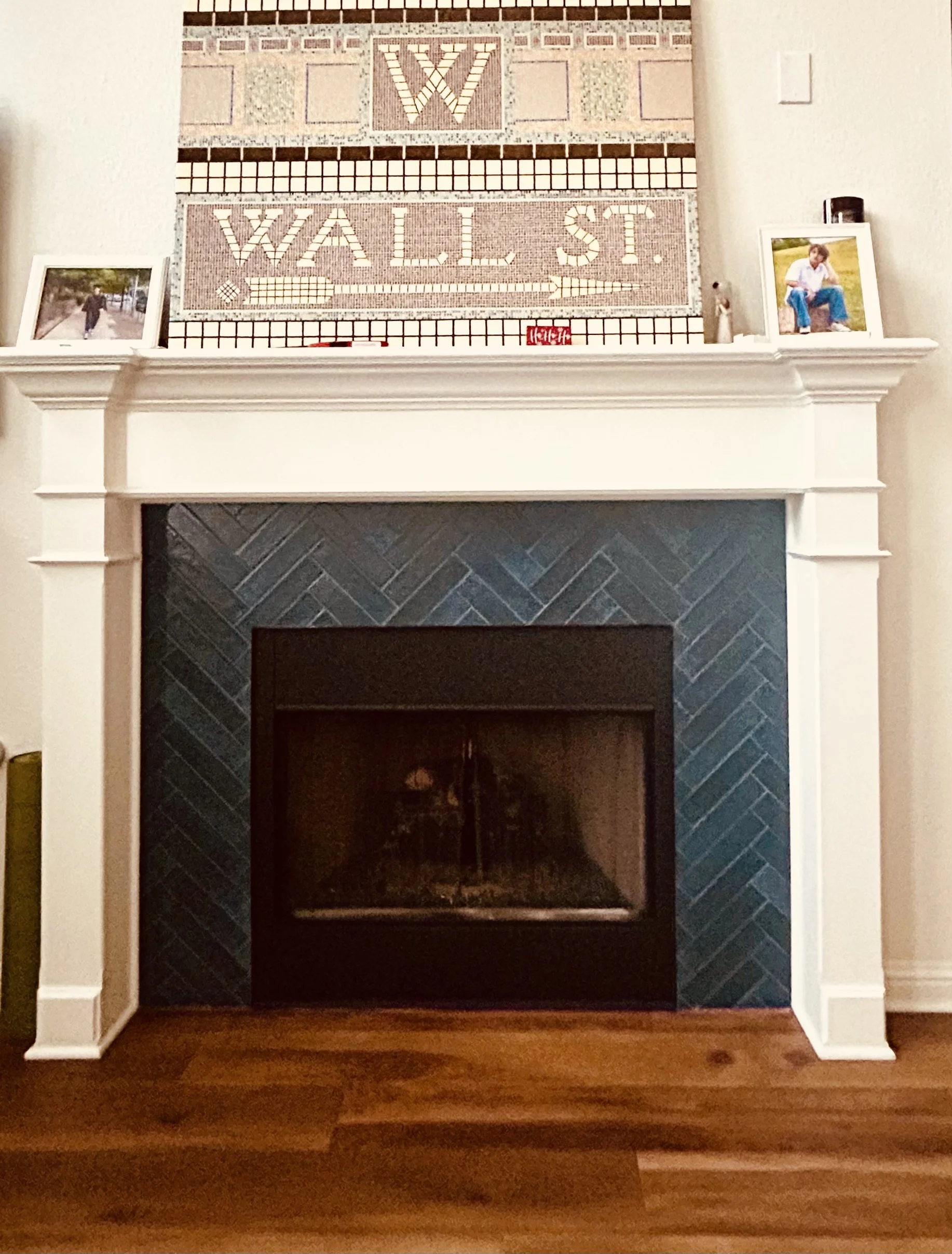 Herringbone tile blue fireplace. Two framed photographs are placed on each side of the mantle, and the fireplace is surrounded by white molding.
