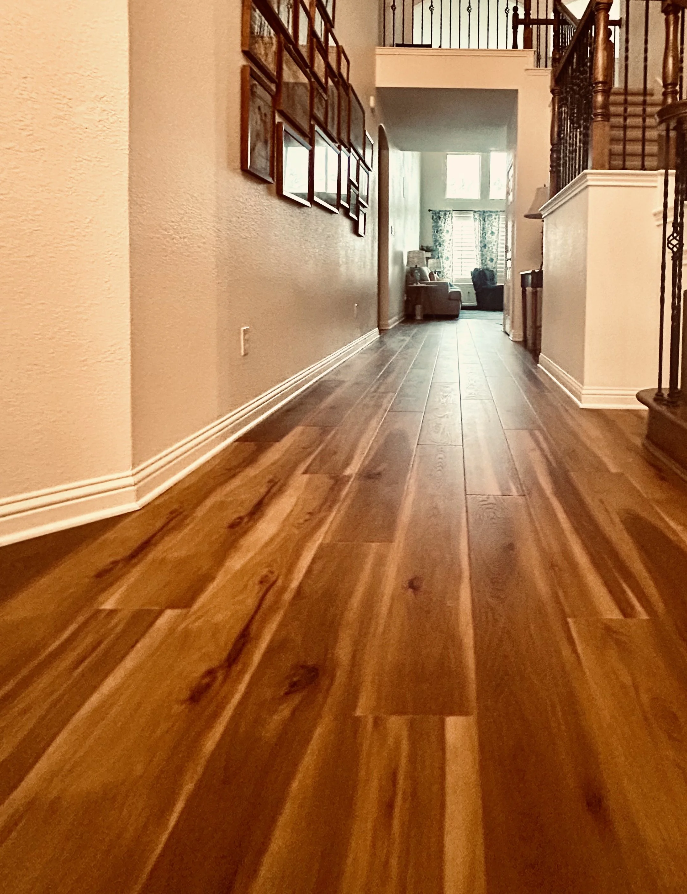 A hallway with wood LVP flooring leading to a sunlit living room at the end, decorated with patterned curtains and furniture.