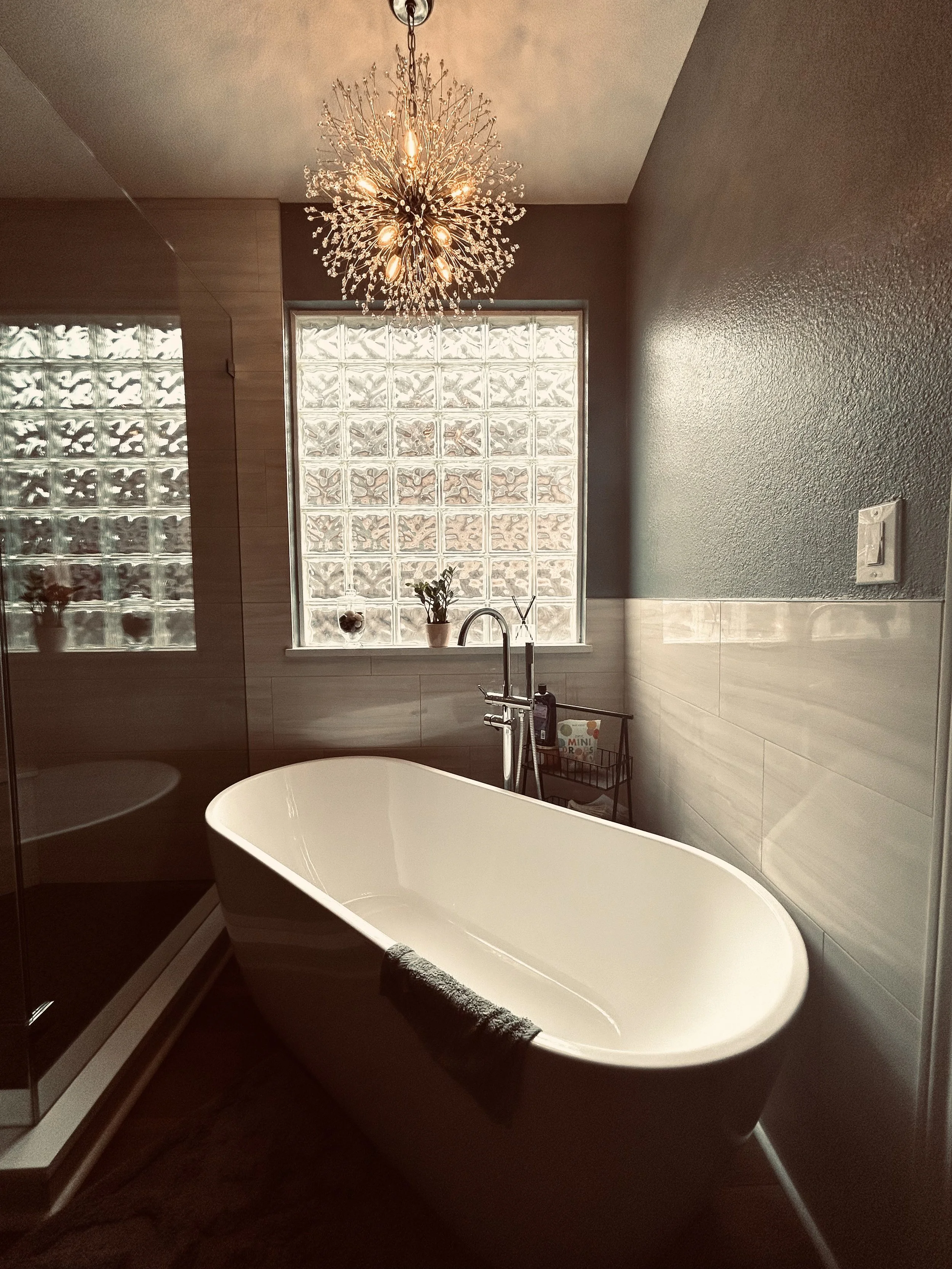 Modern bathroom with freestanding bathtub, glass block window, and decorative chandelier light fixture.