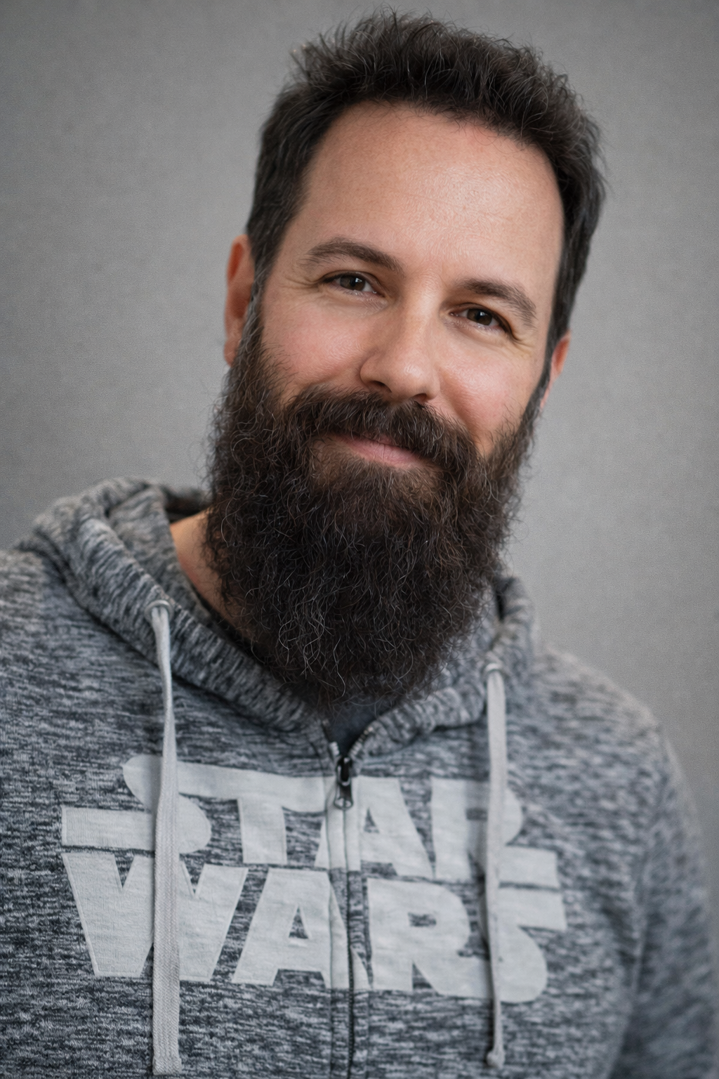 A smiling man with a thick beard and short dark hair wearing a gray hoodie with a 'Star Wars' logo.