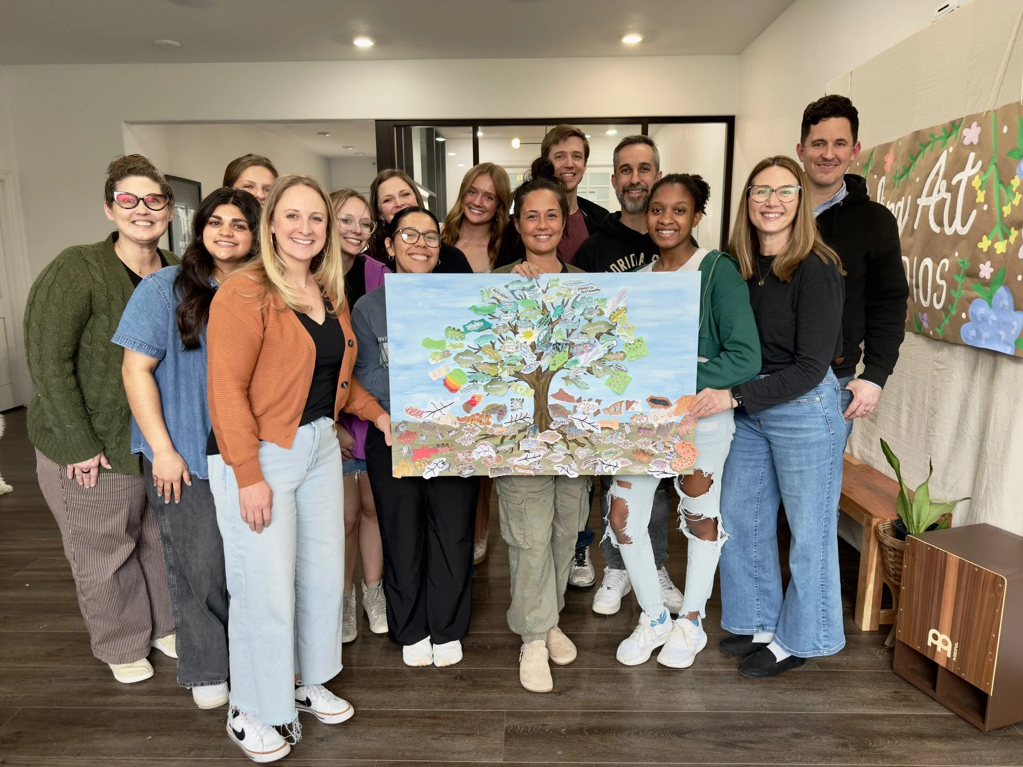 A group of people posing together indoors, holding a colorful tree diagram, smiling at the camera.