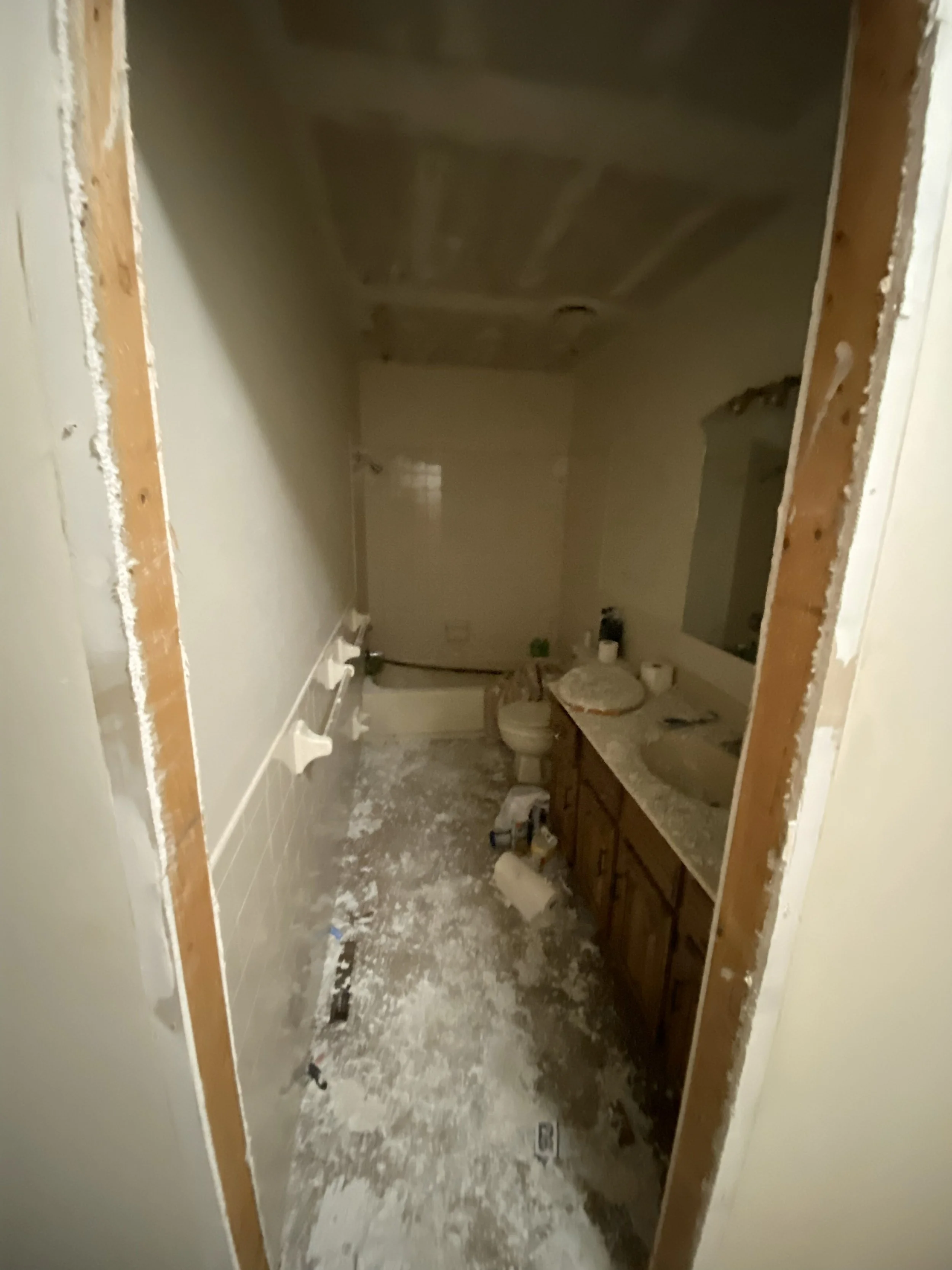 Bathroom under renovation with drywall removed from walls, a countertop sink, toilet, and construction debris on the floor.