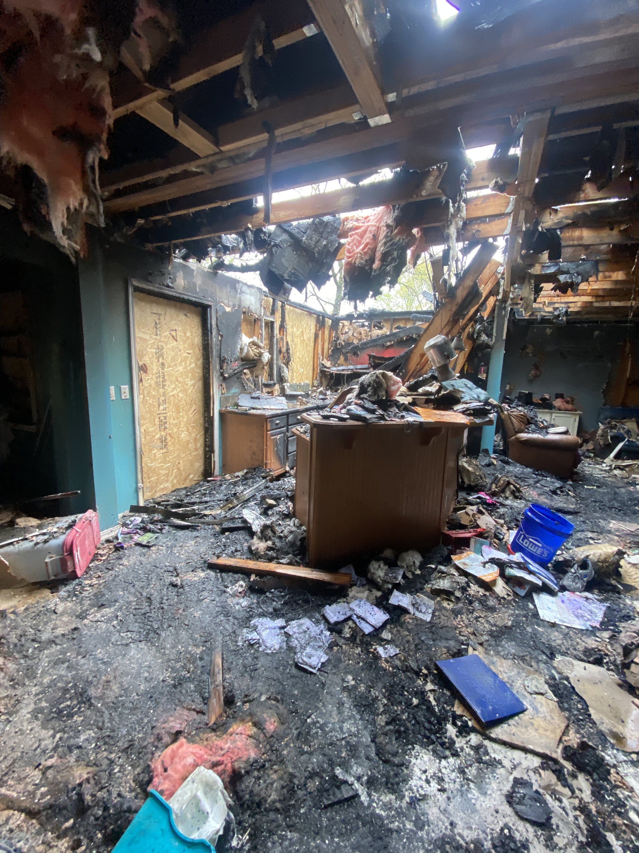 Interior of a house that has been severely damaged by fire, with burnt and charred walls, ceiling, and furniture, and debris scattered across the floor.