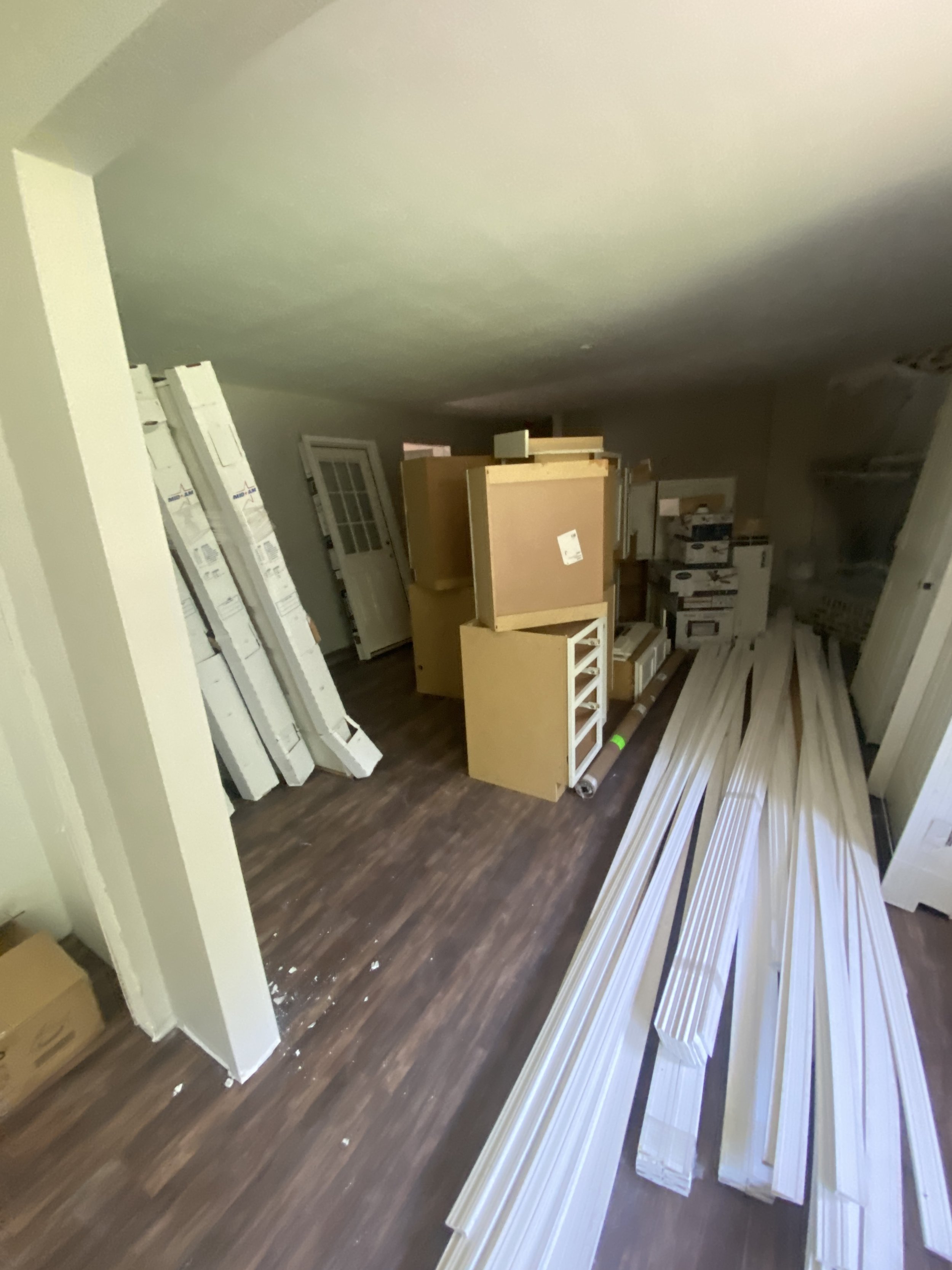 Room filled with construction materials including white framing lumber, boxes, and furniture pieces arranged in the space.