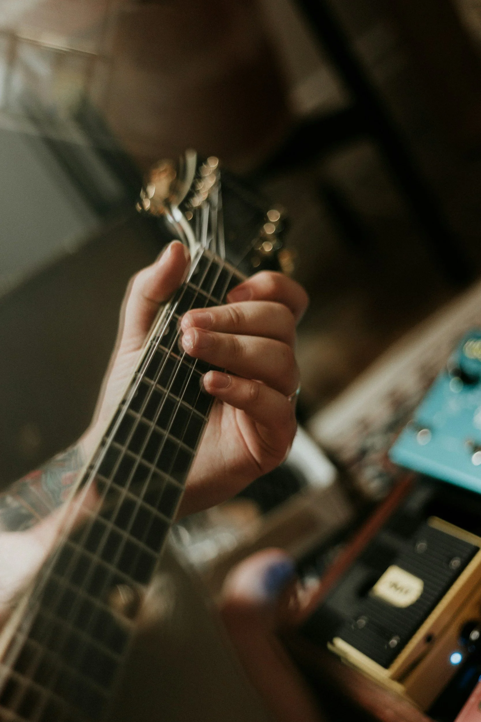 Close-up of a person playing a guitar, showing their hand on the fretboard, with guitar tuning pegs visible in the background.