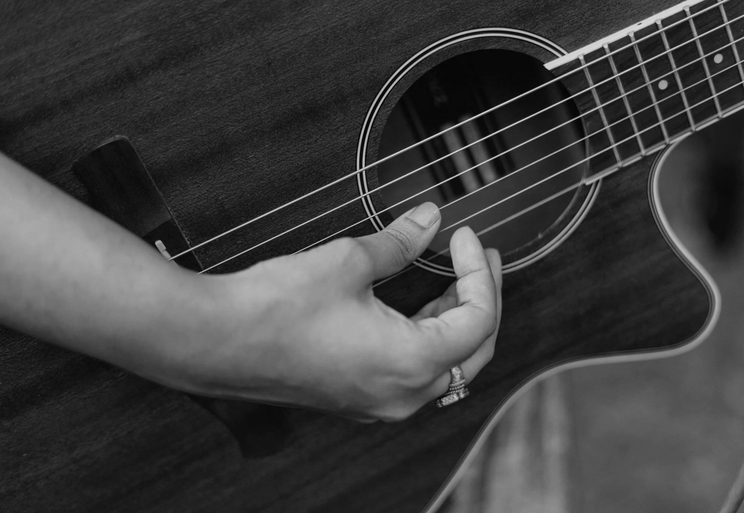 Close-up of a person’s hand pressing on the strings of an acoustic guitar, black and white photo.