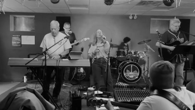 A band performing live music on stage with a keyboard, guitar, drums, and vocals, in an indoor venue.