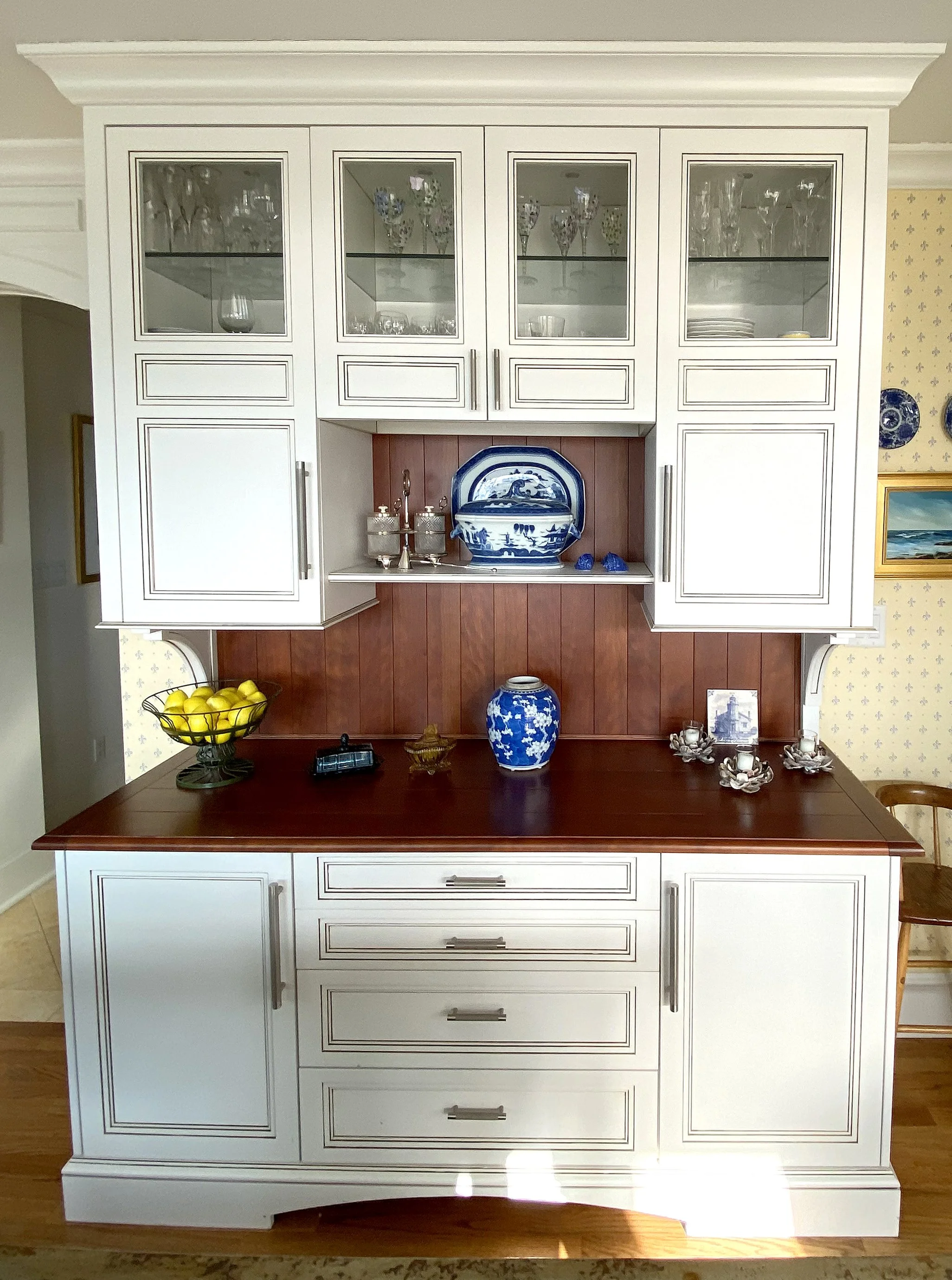 A kitchen hutch with white cabinets and wood accents displaying glassware, decorative dishes, a bowl of lemons, and various decorative items.