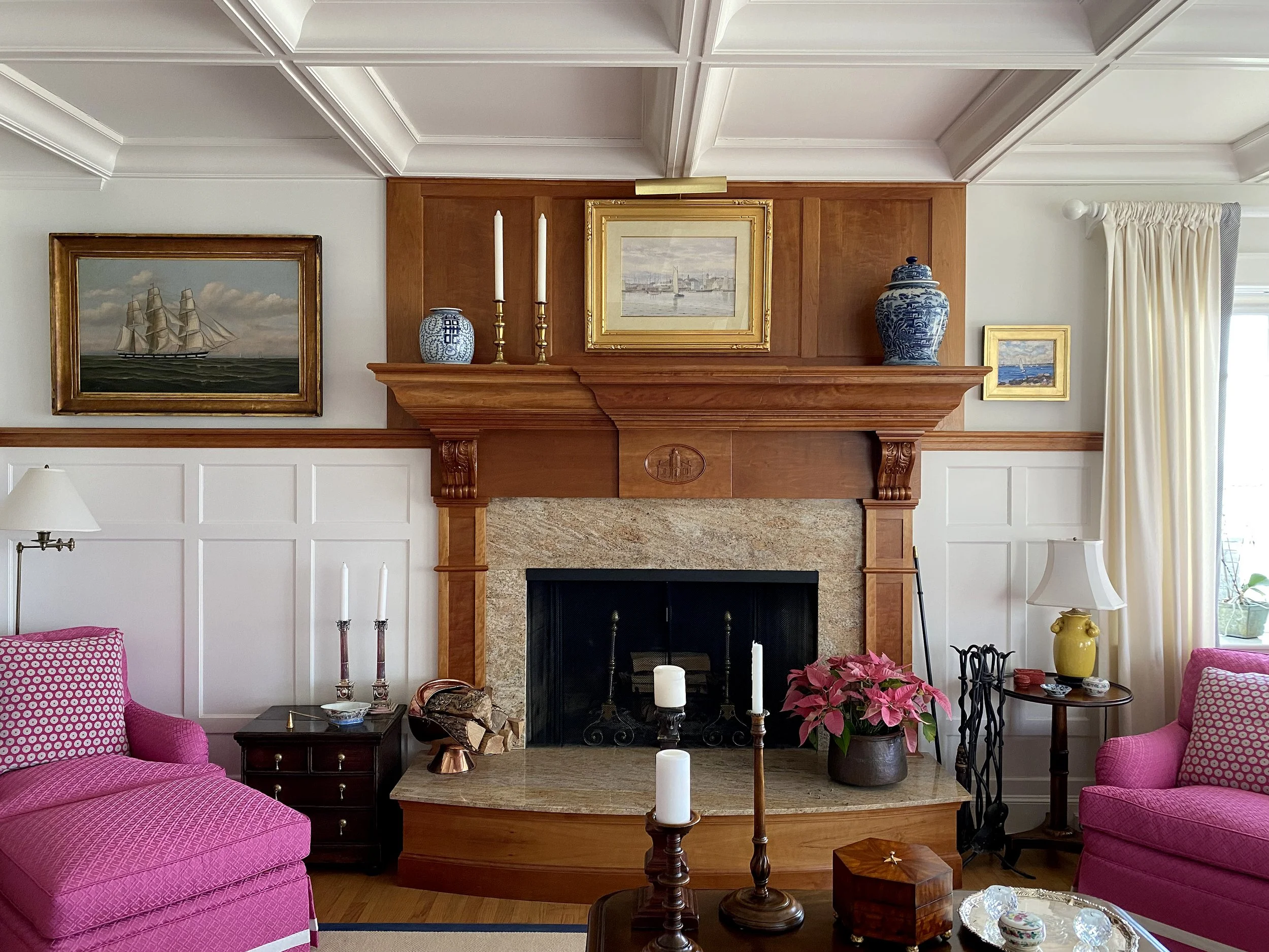 Living room with a fireplace, pink armchairs, and various decorative items, including paintings, vases, candles, and poinsettia plant.