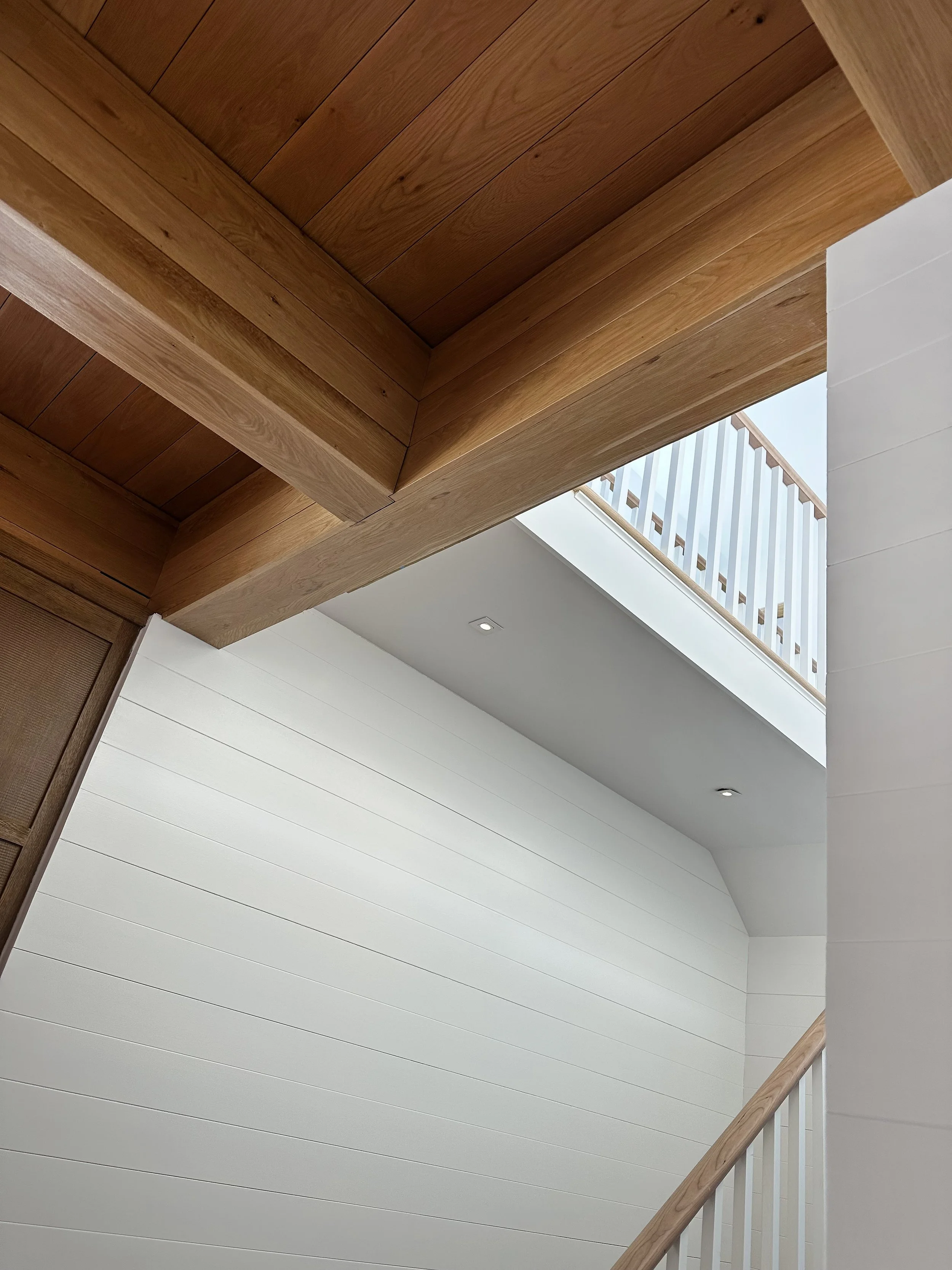 Interior view of a stairwell with white paneled walls, wooden beams, and a frosted glass railing.