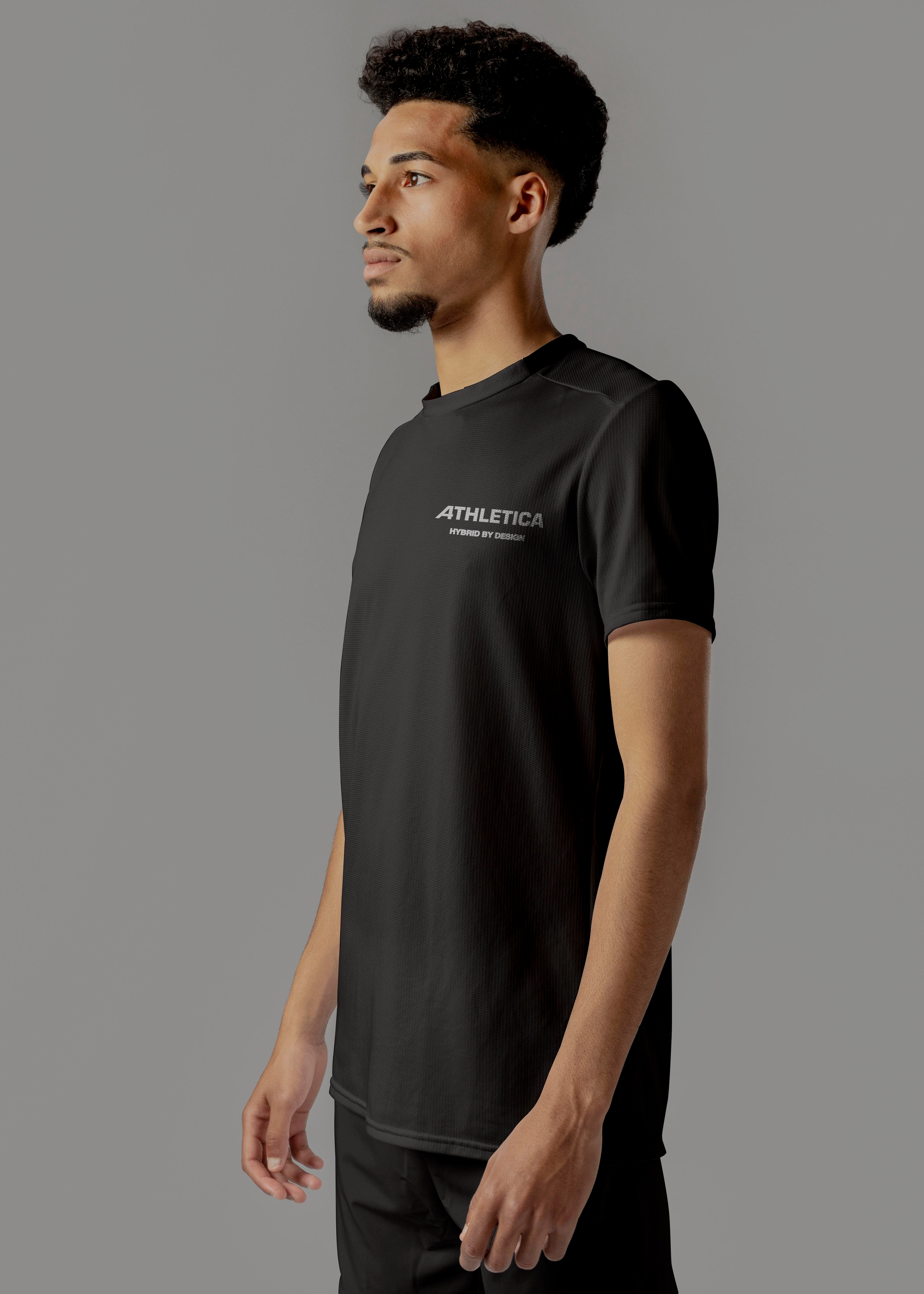 A young man in black athletic wear standing against a gray background, looking to the side. His shirt has the word 'ATHLETICA' and 'HYBRID BY DESIGN' printed on it.