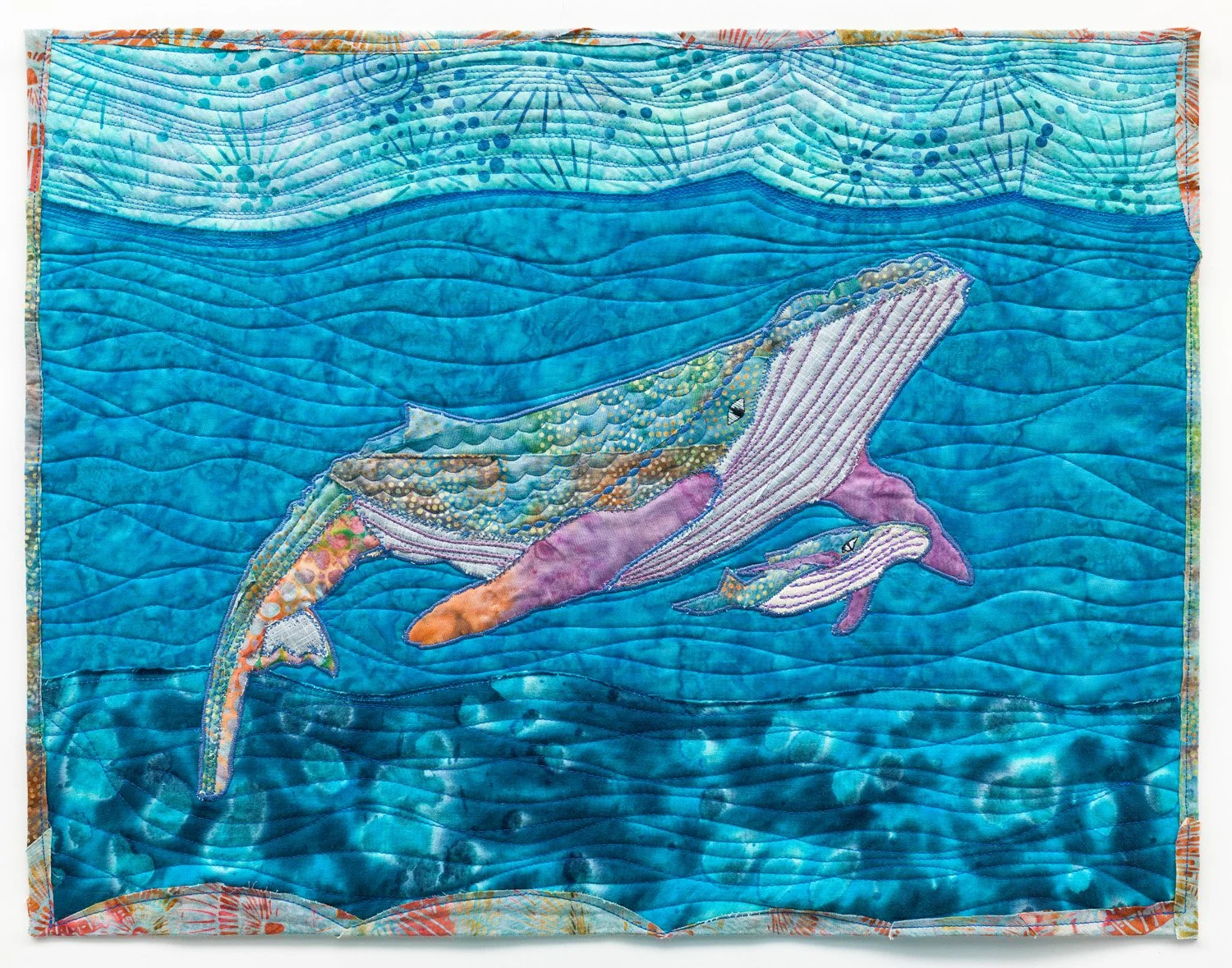 A quilted textile artwork depicting three whales swimming in the ocean, with a blue background and detailed stitching.