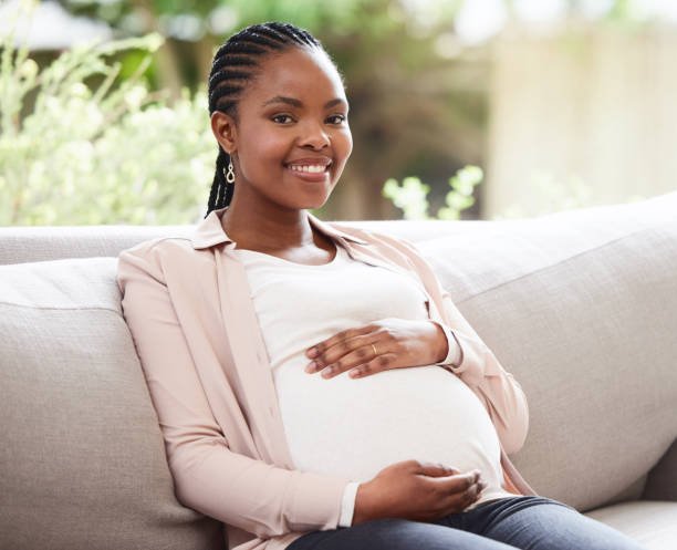 Pregnant woman sitting on a sofa outdoors, smiling, with hands on her belly.