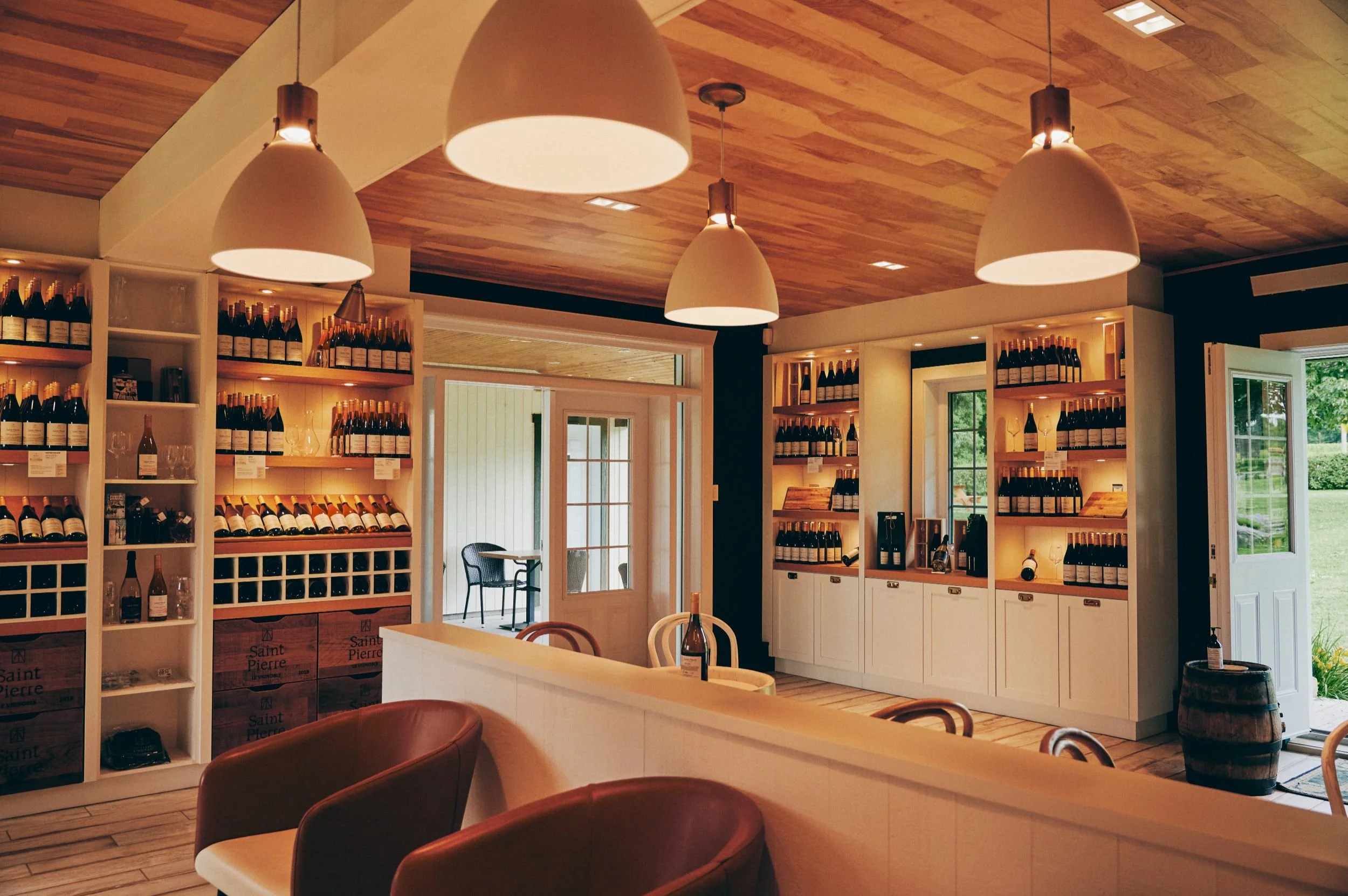 Vue intérieur de la boutique avec des étagères remplies de bouteilles de vin et un espace de dégustation, éclairée par des lampes suspendues au plafond en bois.