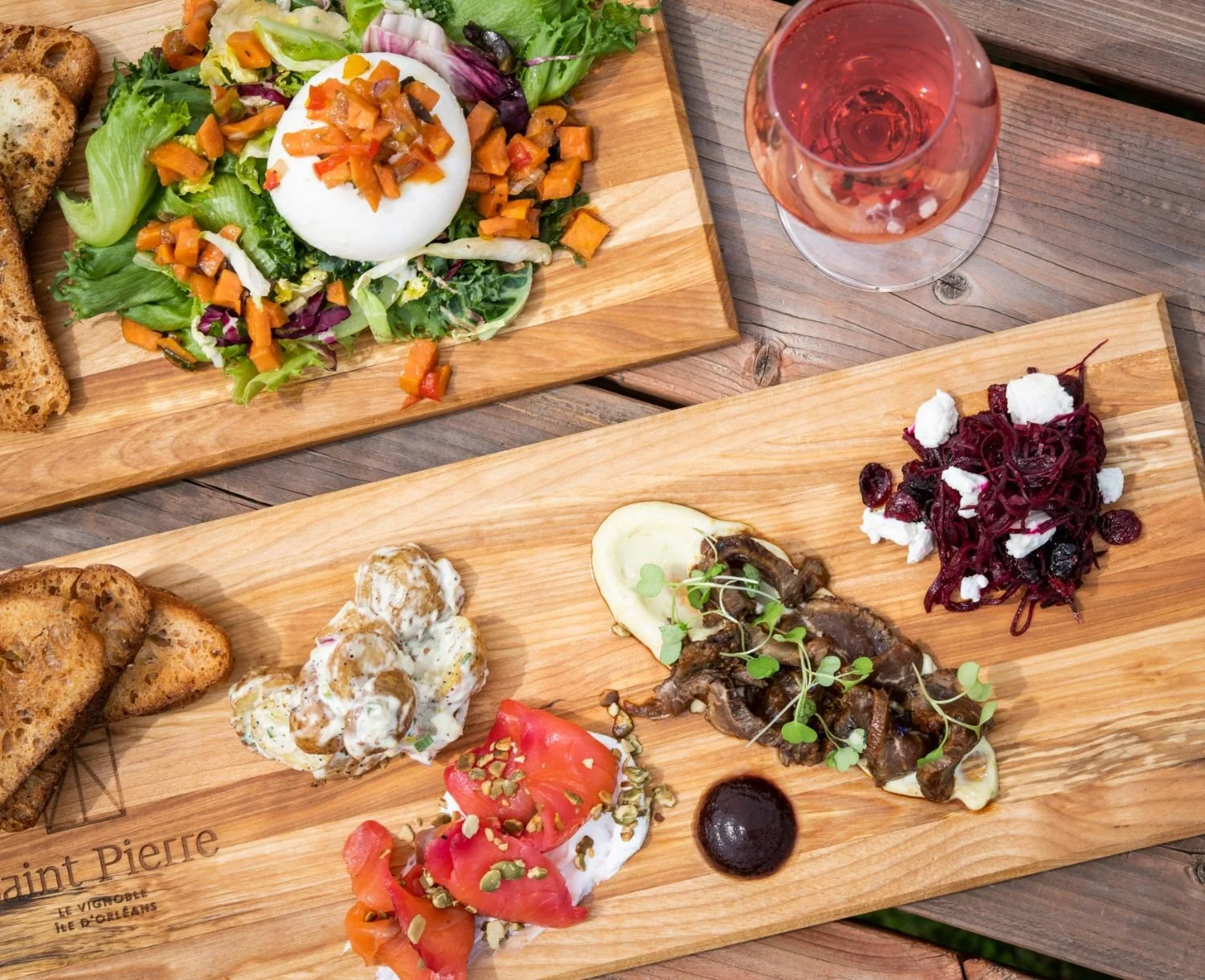 Deux planches en bois avec des plats appétissants: une salade avec œuf mollet et légumes, un assortiment de tartines, avec salade et un verre de vin rosé sur une table en bois