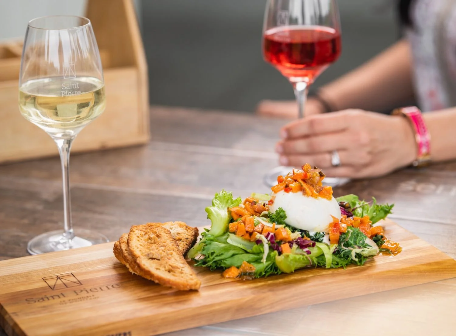 Salade avec œuf mollet, légumes et toast, servie sur une planche en bois, accompagné de verre de vin blanc et verre de vin rosé.