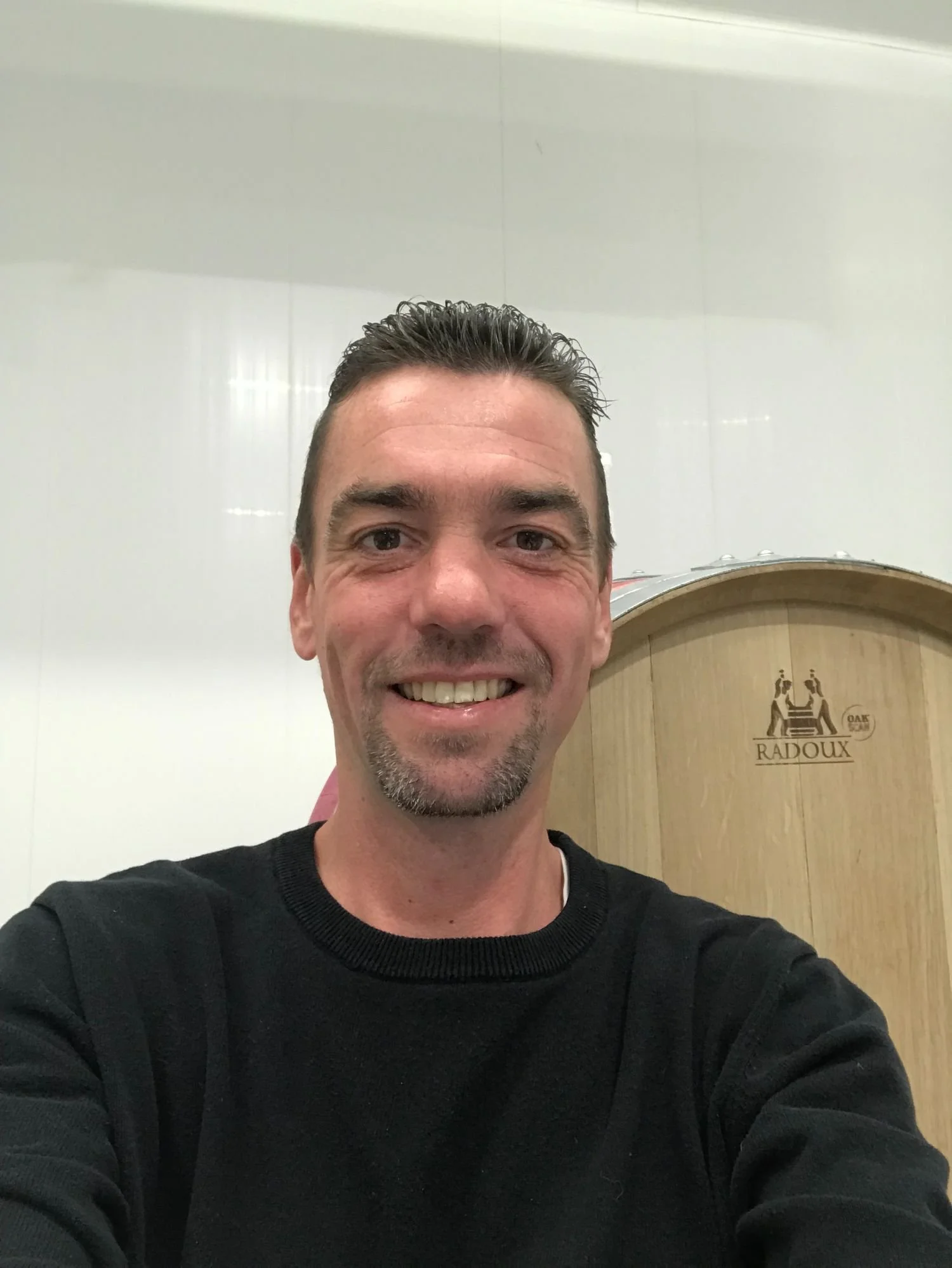 Un homme souriant dans une pièce blanche, avec un équipement de vin en arrière-plan.