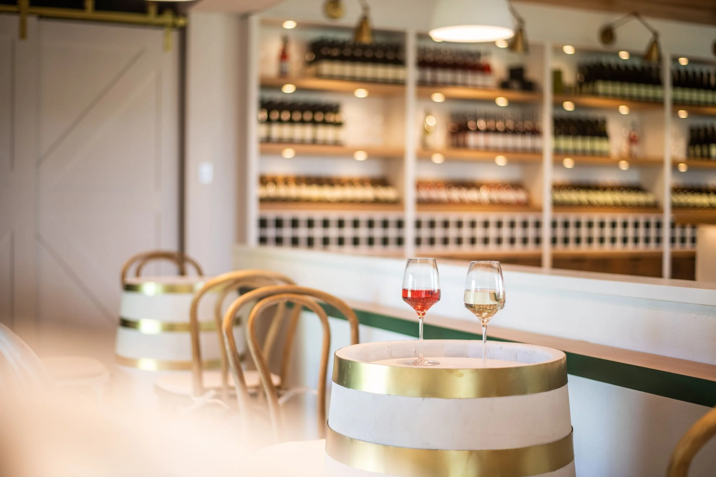 Deux verres de vin rouge et blanc sur une table en forme de barrique à l'intérieur de la boutique Saint-Pierre le Vignoble, avec étagères de bouteilles en arrière-plan.