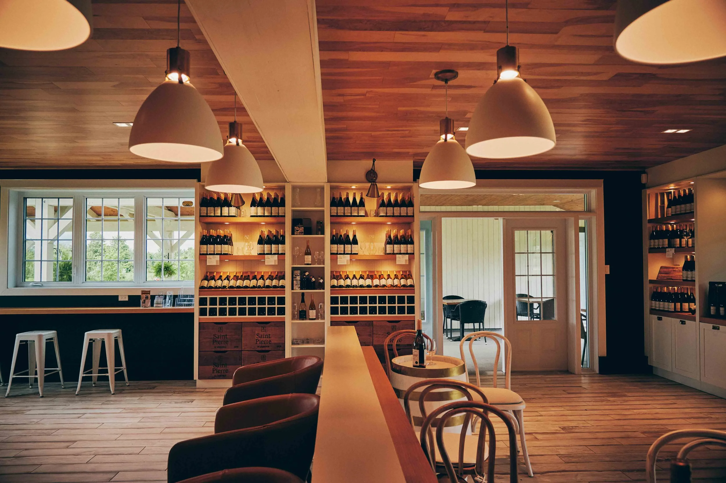 Intérieur du vignoble présentant des étagères de bouteilles de vin, tables, chaises, grande fenêtre et lumière suspendue